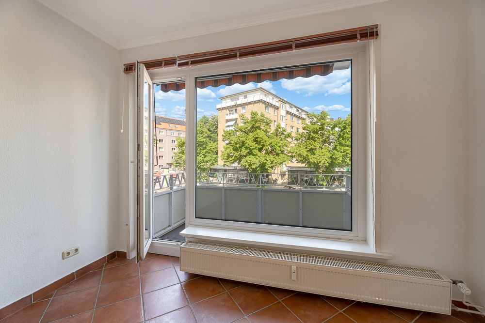 Helles Zimmer mit offenem Fenster, Blick auf Balkon und Wohngebäude im Hintergrund.