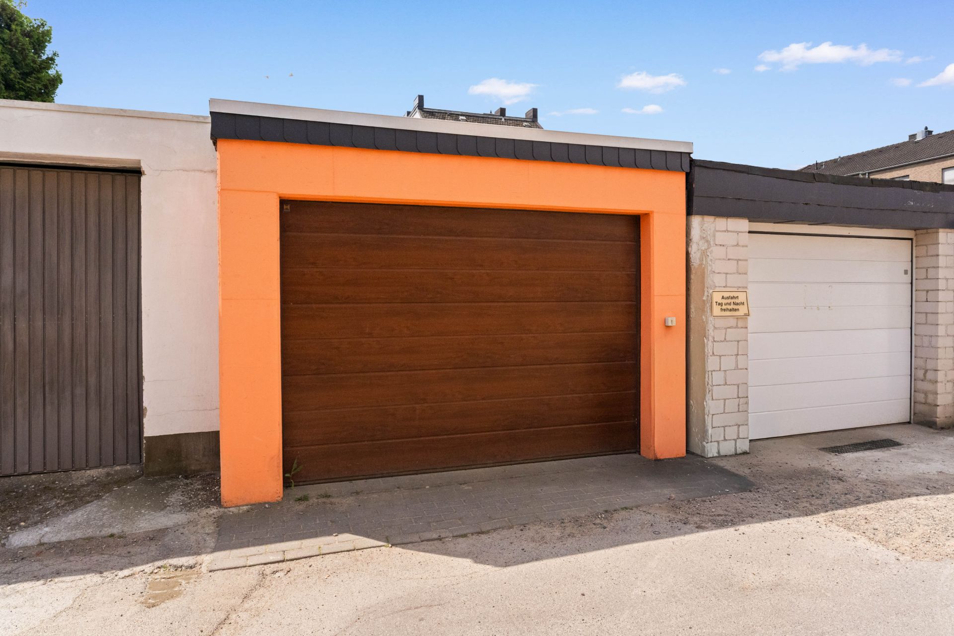 Garage mit braunem Tor und orangefarbenem Rahmen neben weißer Garage.