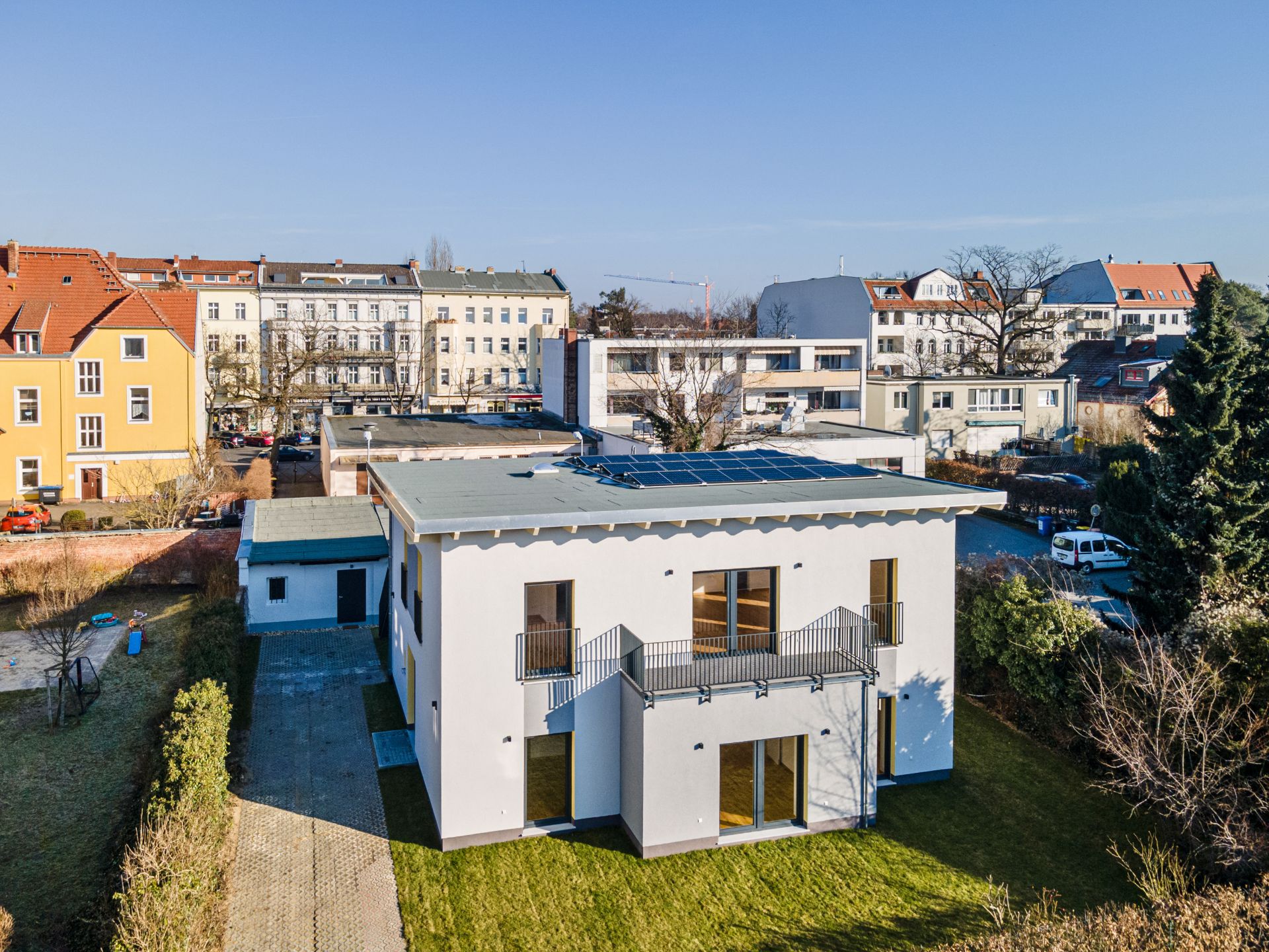 Modernes, zweistöckiges Wohnhaus mit Balkon und Solarpaneelen auf dem Dach, umgeben von Garten.