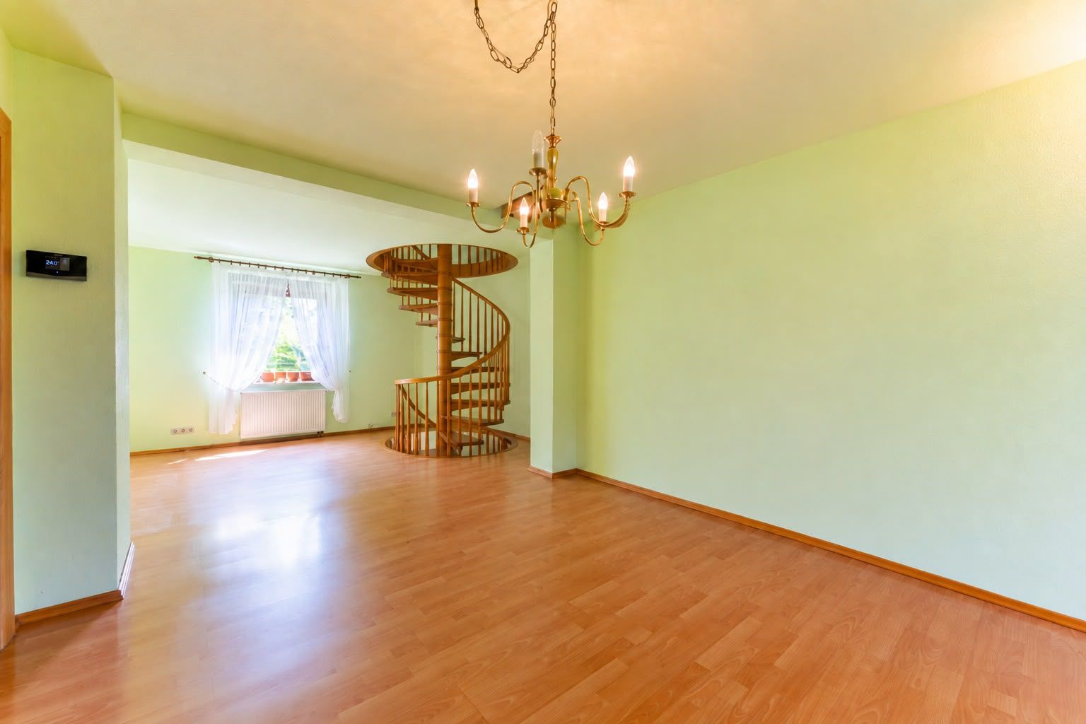 Leerer Raum mit Holzfußboden, Kronleuchter und Wendeltreppe, Fenster mit Gardinen.