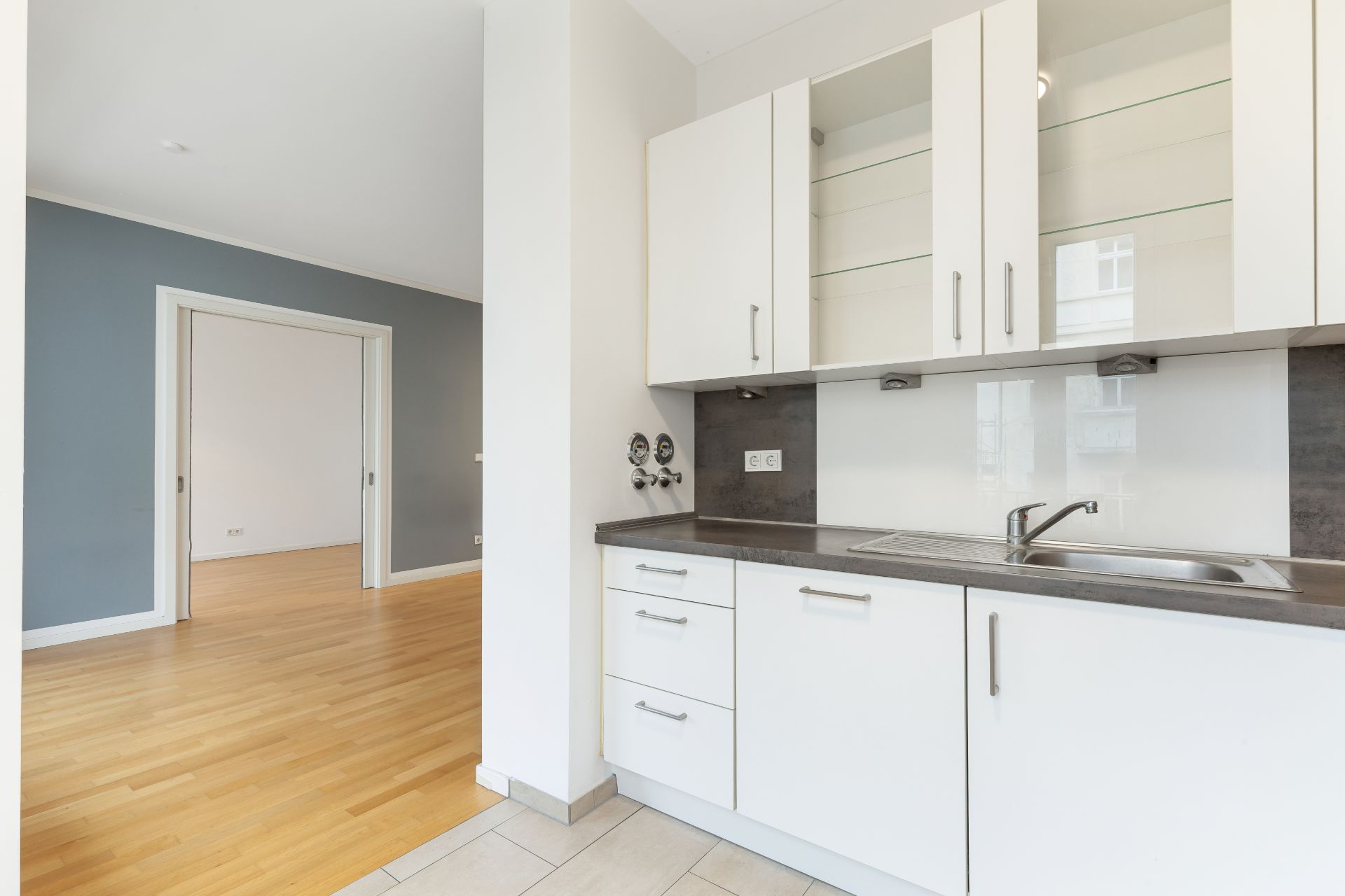 Moderne weiße Einbauküche mit Spüle und Blick in ein Wohnzimmer mit Holzboden.