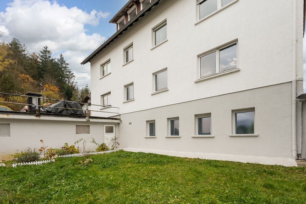 Weiße Wohnhausfassade mit mehreren Fenstern und Rasenfläche im Vordergrund.