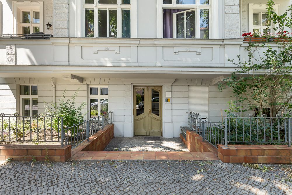 Eingang eines Wohnhauses mit zwei Türen, Fenstern und kleinen bepflanzten Bereichen links und rechts.