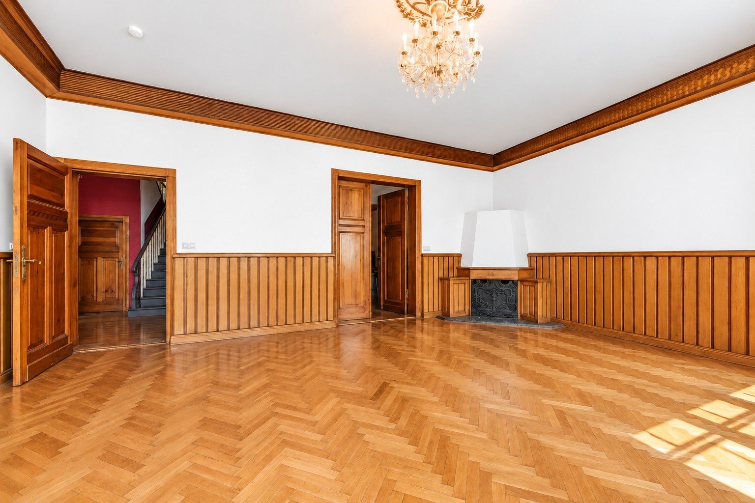 Heller Raum mit Holzboden, Holzvertäfelung, Kamin und Kronleuchter.
