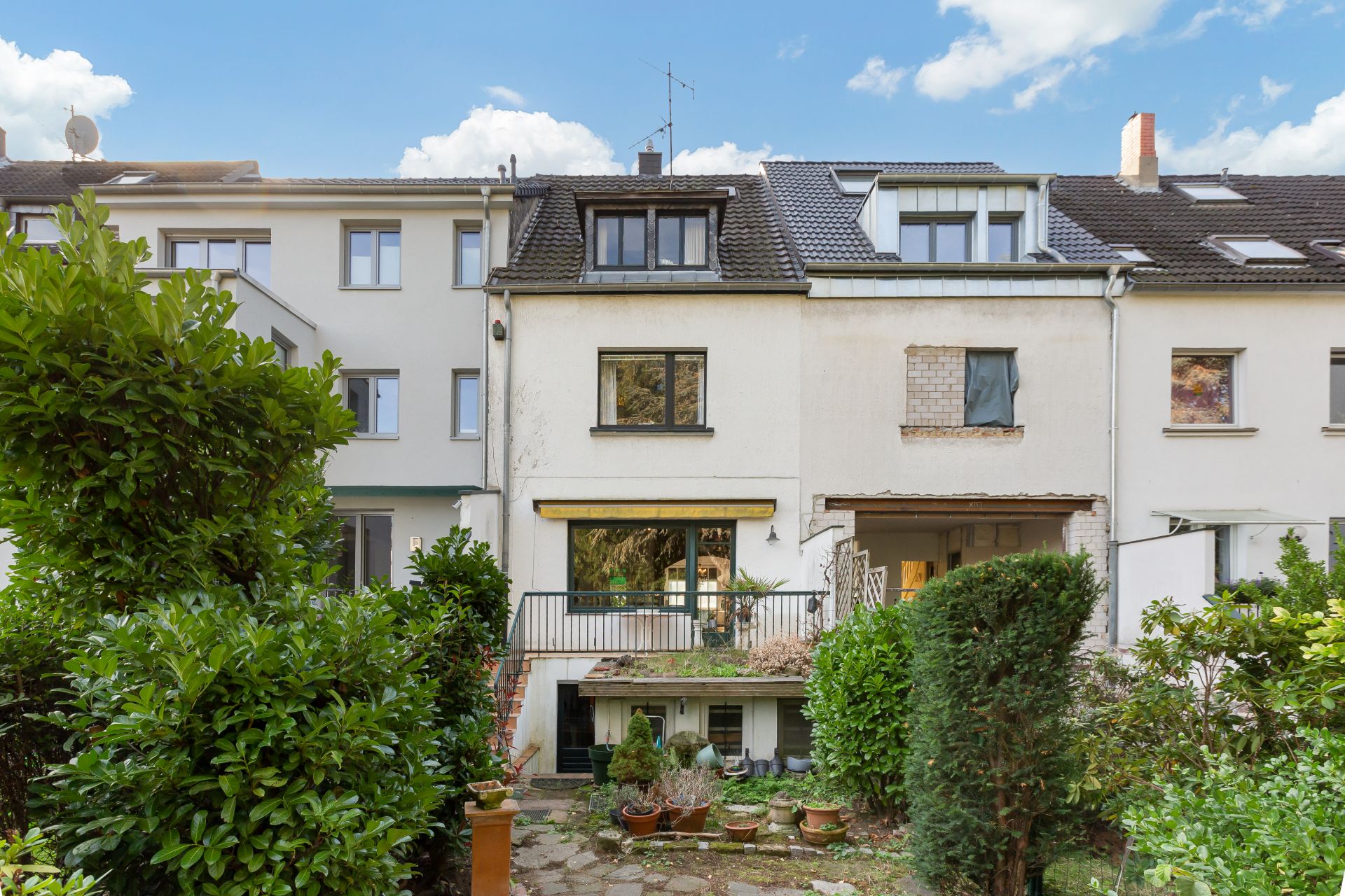 Rückseite eines mehrstöckigen Wohnhauses mit Terrasse, Garten und Pflanzen im Vordergrund.