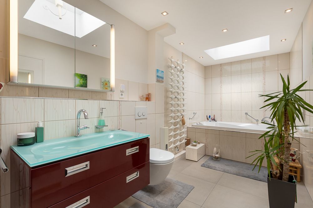 Modernes Badezimmer mit Badewanne, Waschtisch, Spiegel und Pflanze, viel Tageslicht durch Dachfenster.