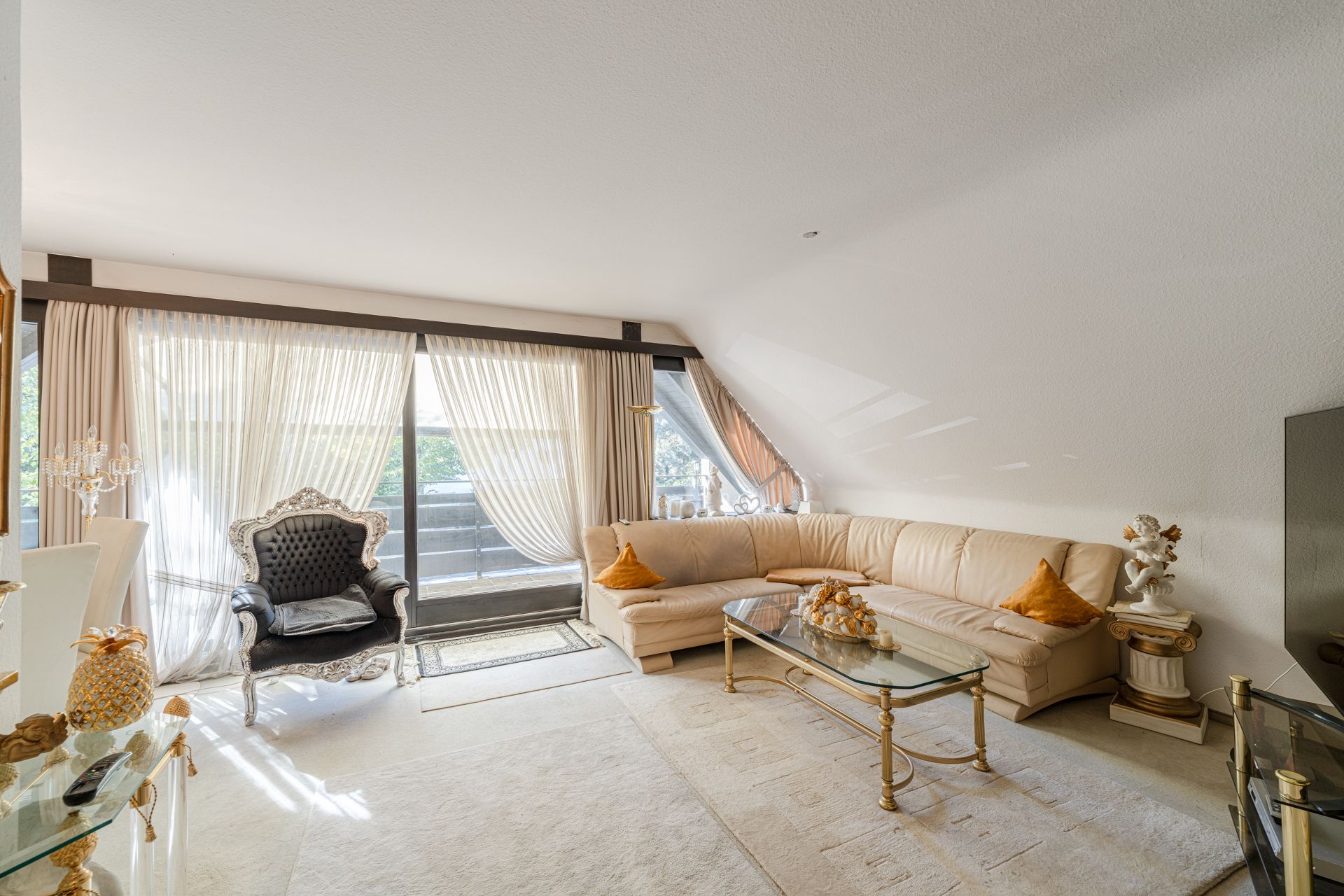 Helles Wohnzimmer mit Ecksofa, Sessel, Glastisch und großen Fenstern mit Vorhängen.