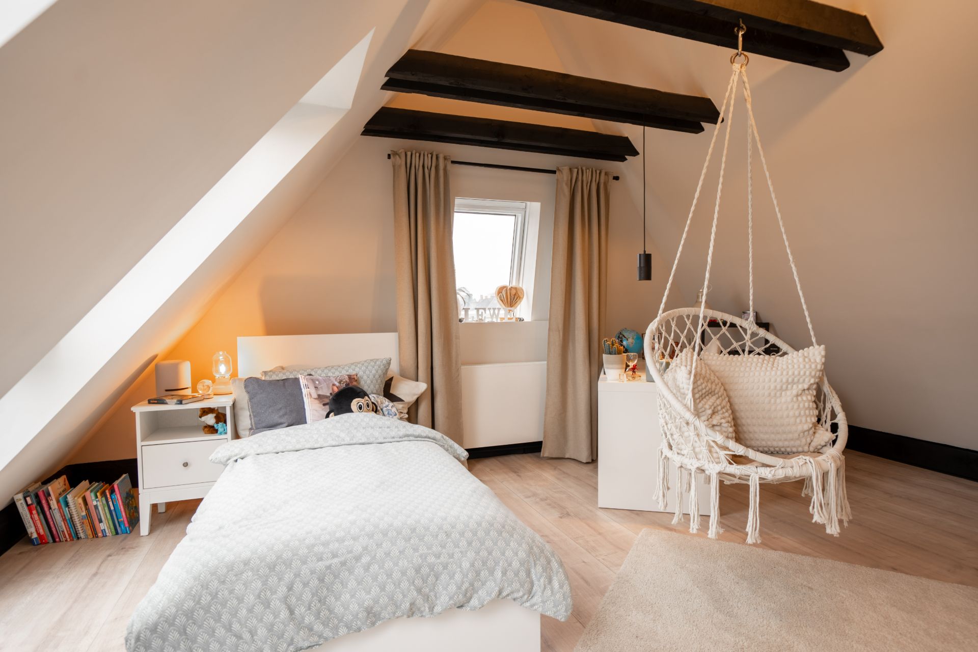Gemütliches Schlafzimmer mit Bett, Nachttisch, Bücherregal und Hängesessel unter Dachschrägen.