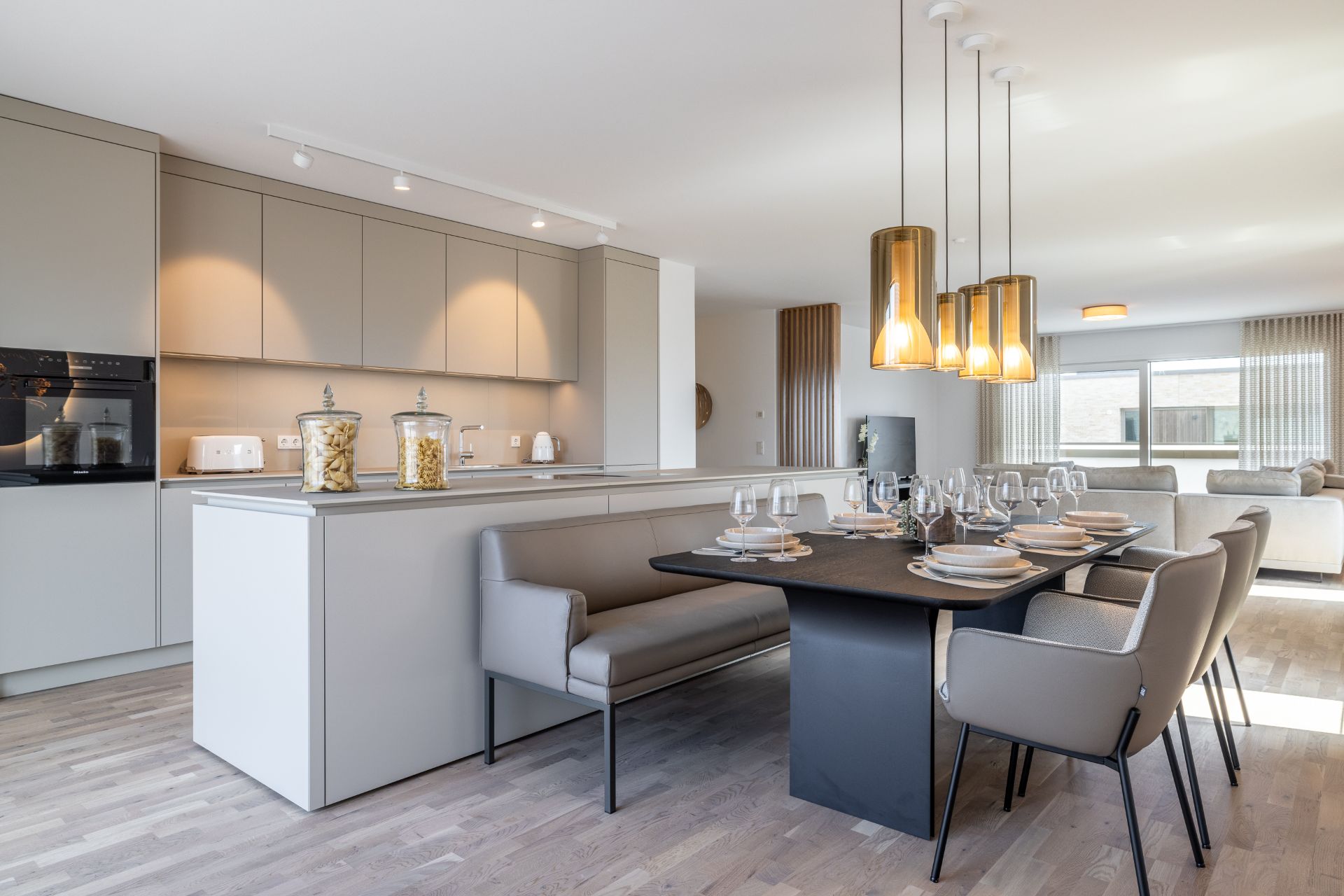 Moderne offene Küche mit Esstisch, Stühlen und Hängelampen in hellem Wohnraum.