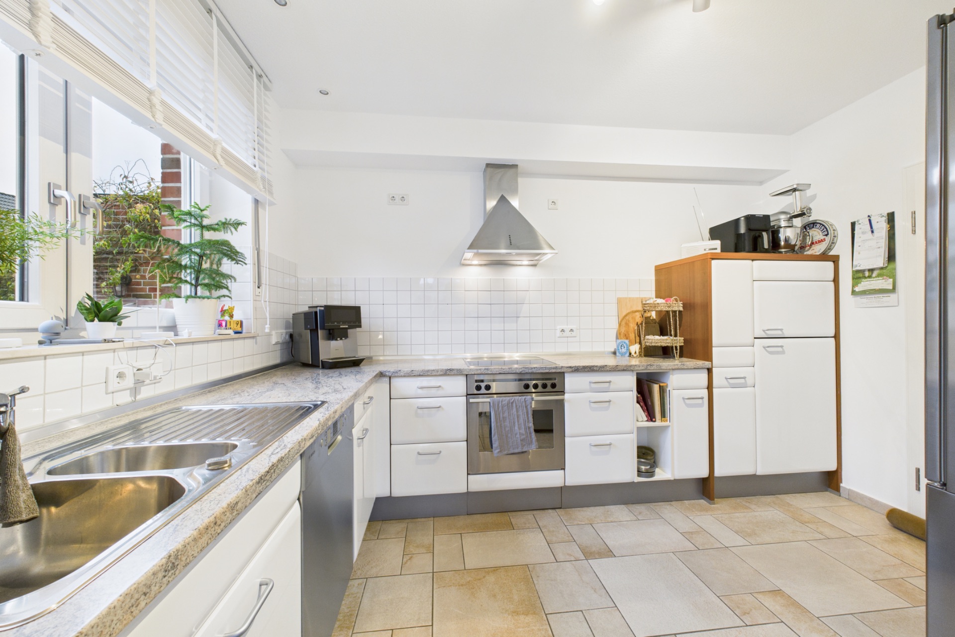 Helle, moderne Einbauküche mit weißen Schränken, Herd, Spüle und Fenster mit Pflanzen.
