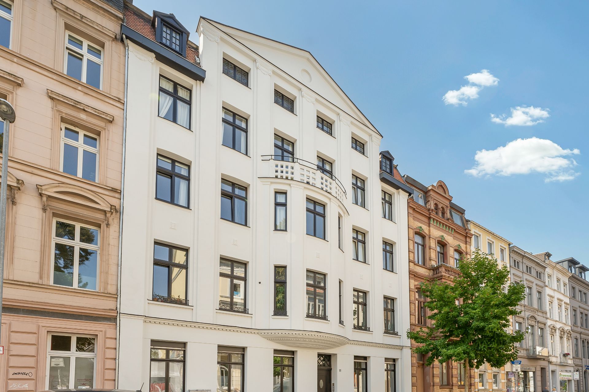 Mehrstöckiges Wohngebäude mit weißer Fassade und schwarzen Fenstern, daneben weitere Häuser.
