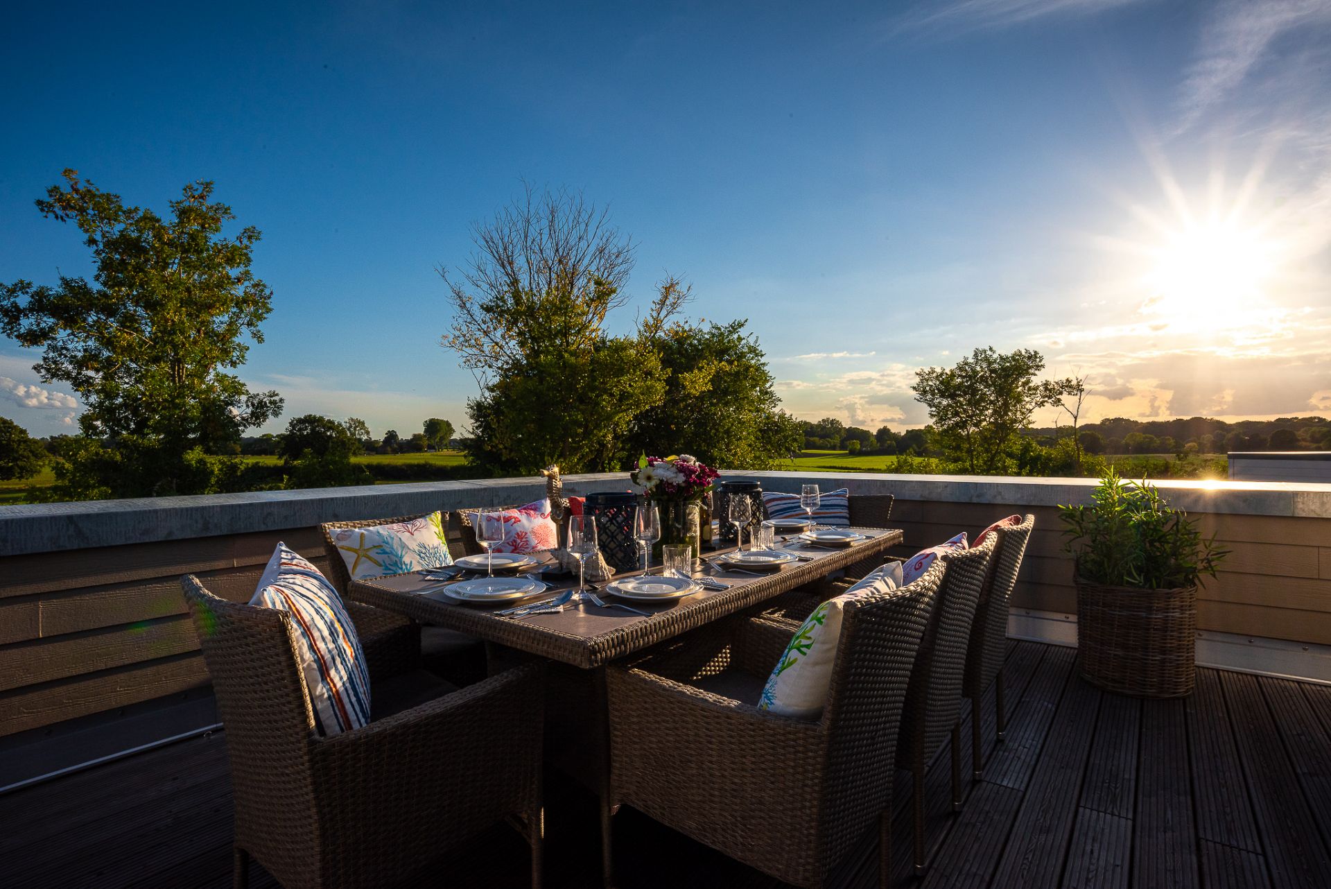 Terrasse mit gedecktem Esstisch, Stühlen mit Kissen und Blick auf grüne Landschaft bei Sonnenuntergang.