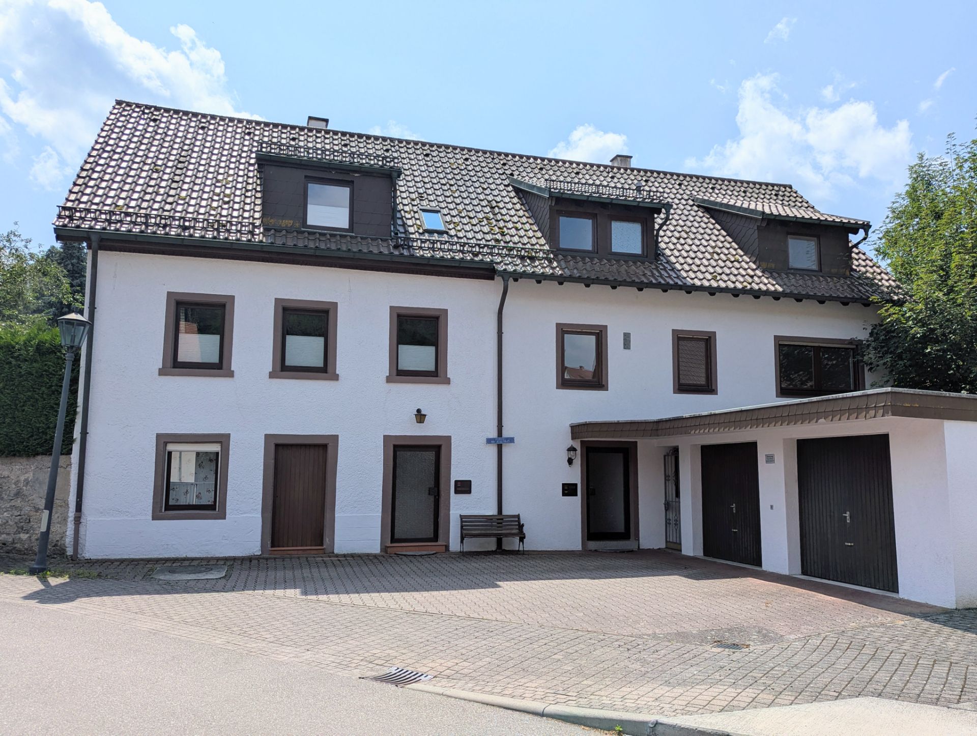 Zweistöckiges Wohnhaus mit weißer Fassade, braunen Fenstern und zwei Garagen.