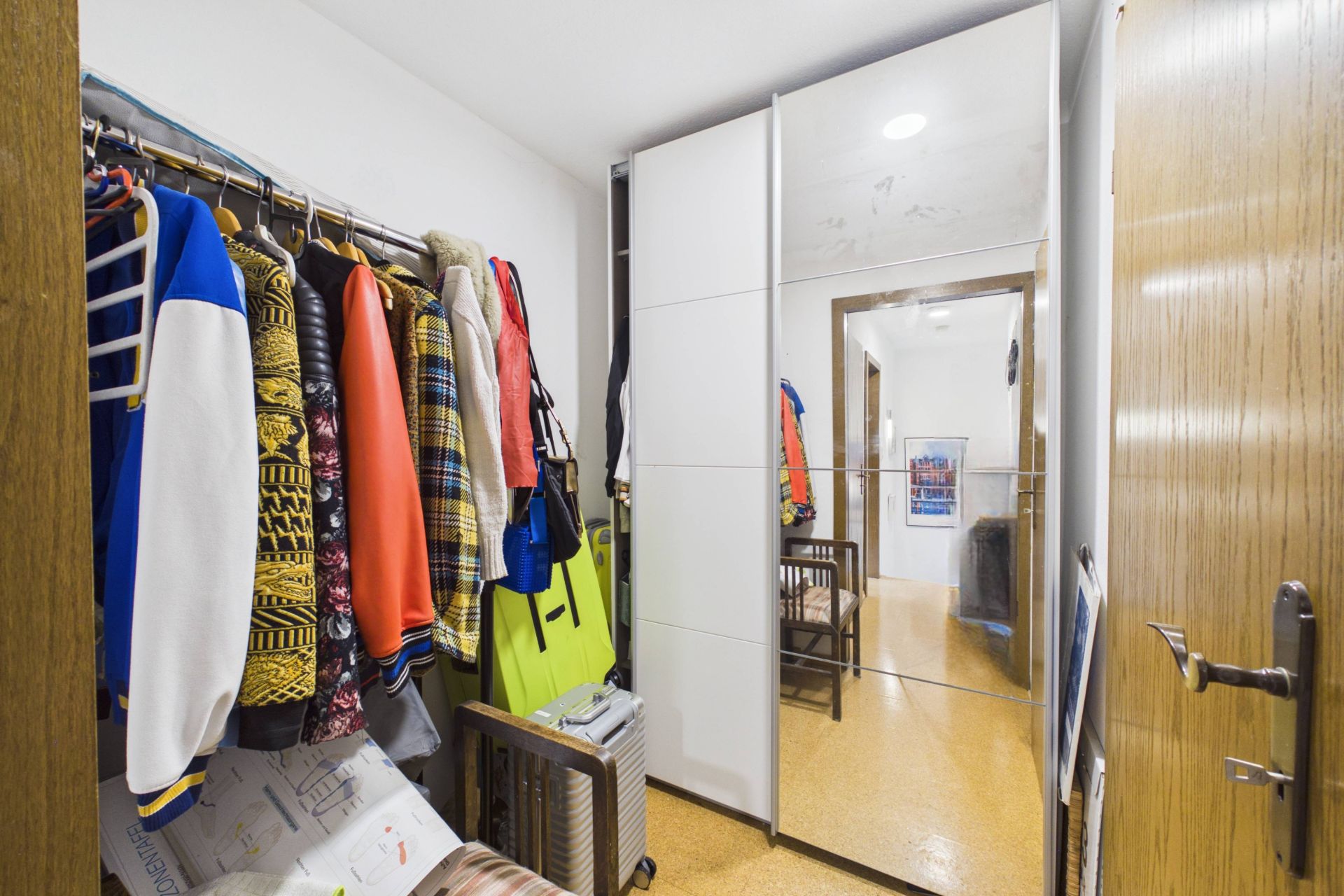 Kleiner Flur mit Kleiderstange, bunten Jacken, Koffer und Spiegelschrank.