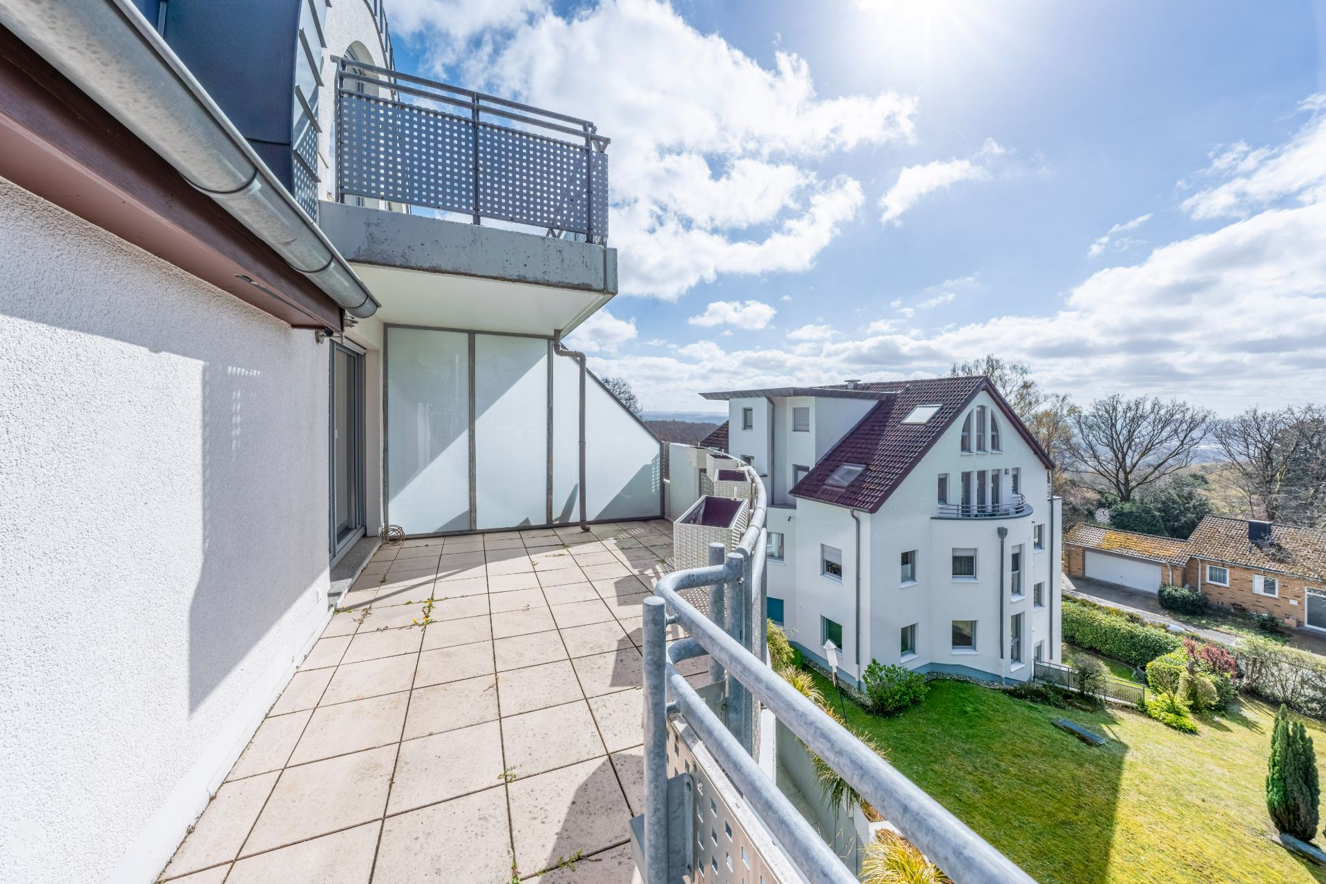 Großer Balkon mit Fliesenboden, Blick auf Nachbarhäuser und Garten bei sonnigem Wetter.
