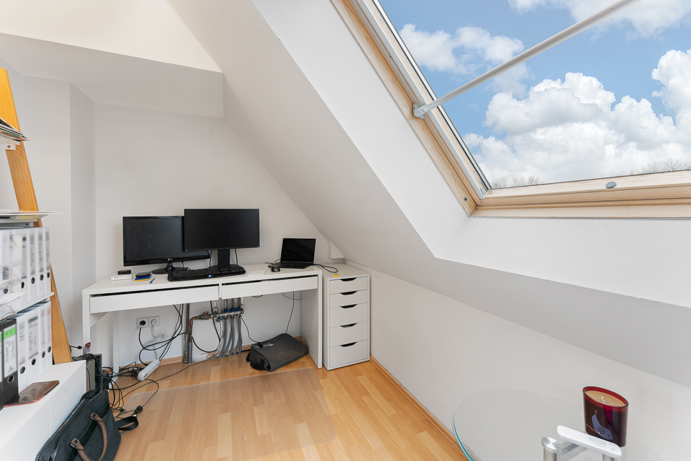 Helles Arbeitszimmer mit Schreibtisch, zwei Monitoren und großem Dachfenster unter einer Schräge.