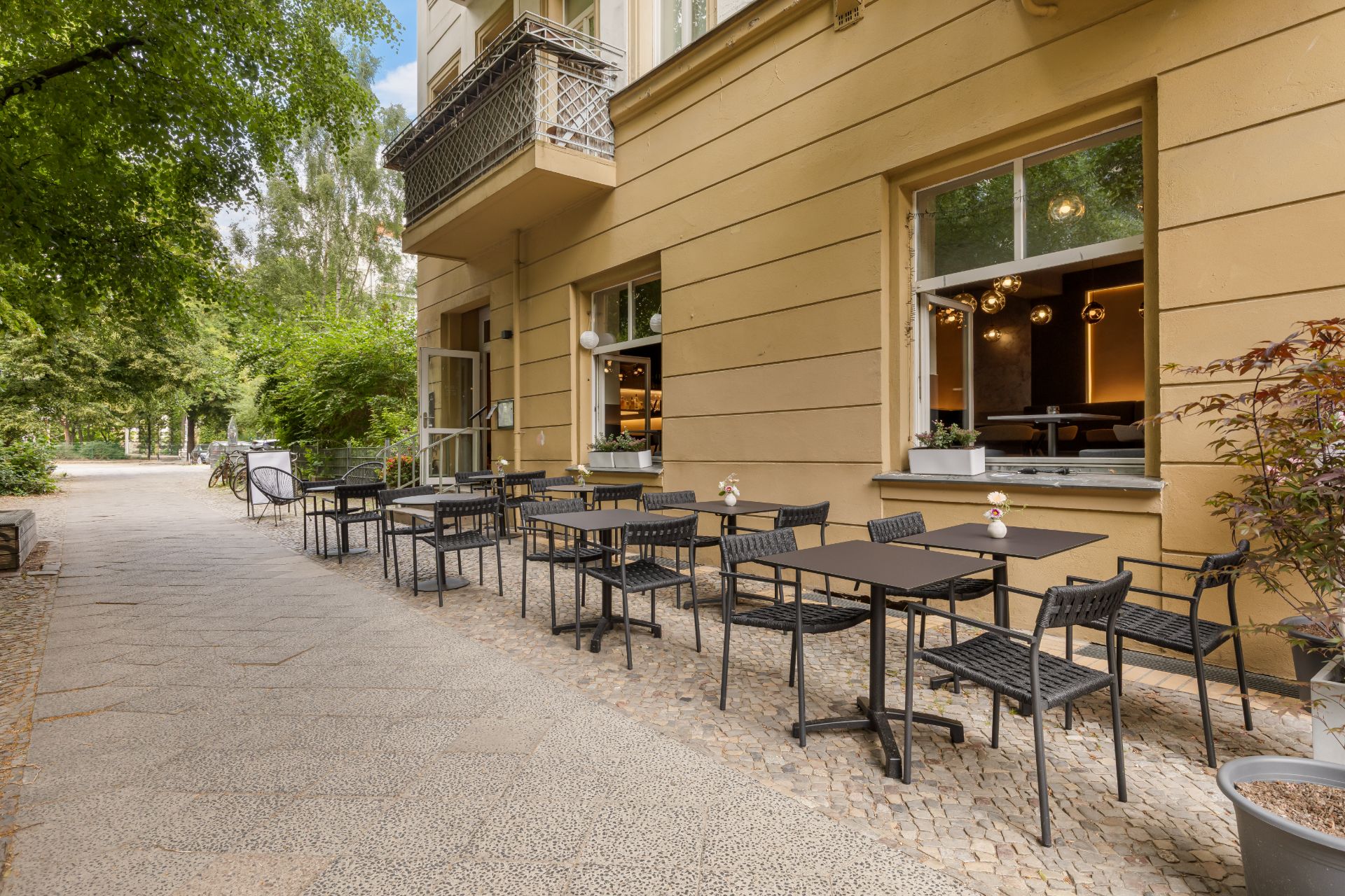 Mehrere Tische und Stühle stehen auf einer Terrasse vor einem gelben Wohngebäude.