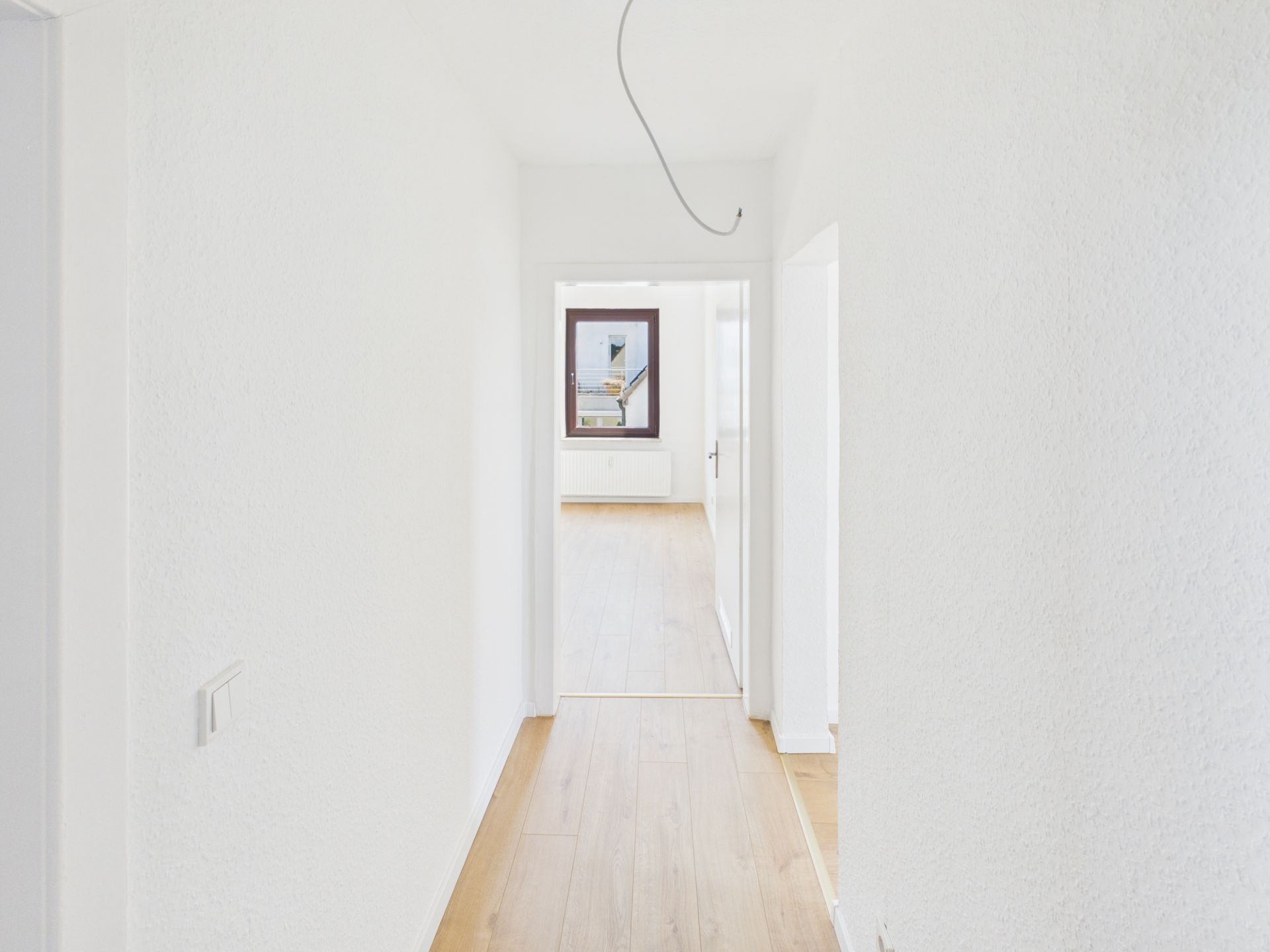 Heller Flur mit weiß gestrichenen Wänden und hellem Holzboden, Blick in ein weiteres Zimmer.