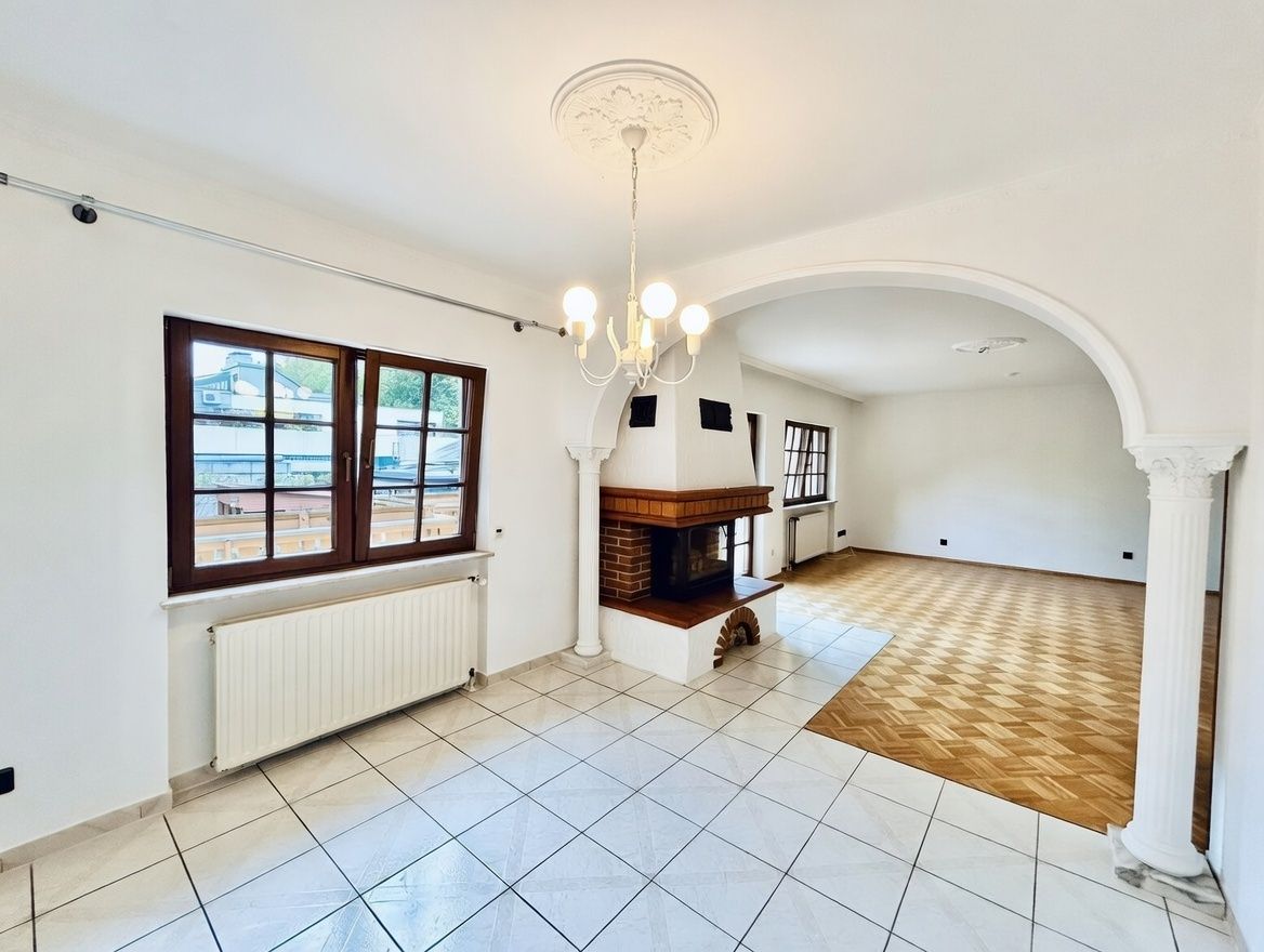 Helles Wohnzimmer mit Kamin, Fliesen- und Parkettboden, großem Fenster und Rundbogen.