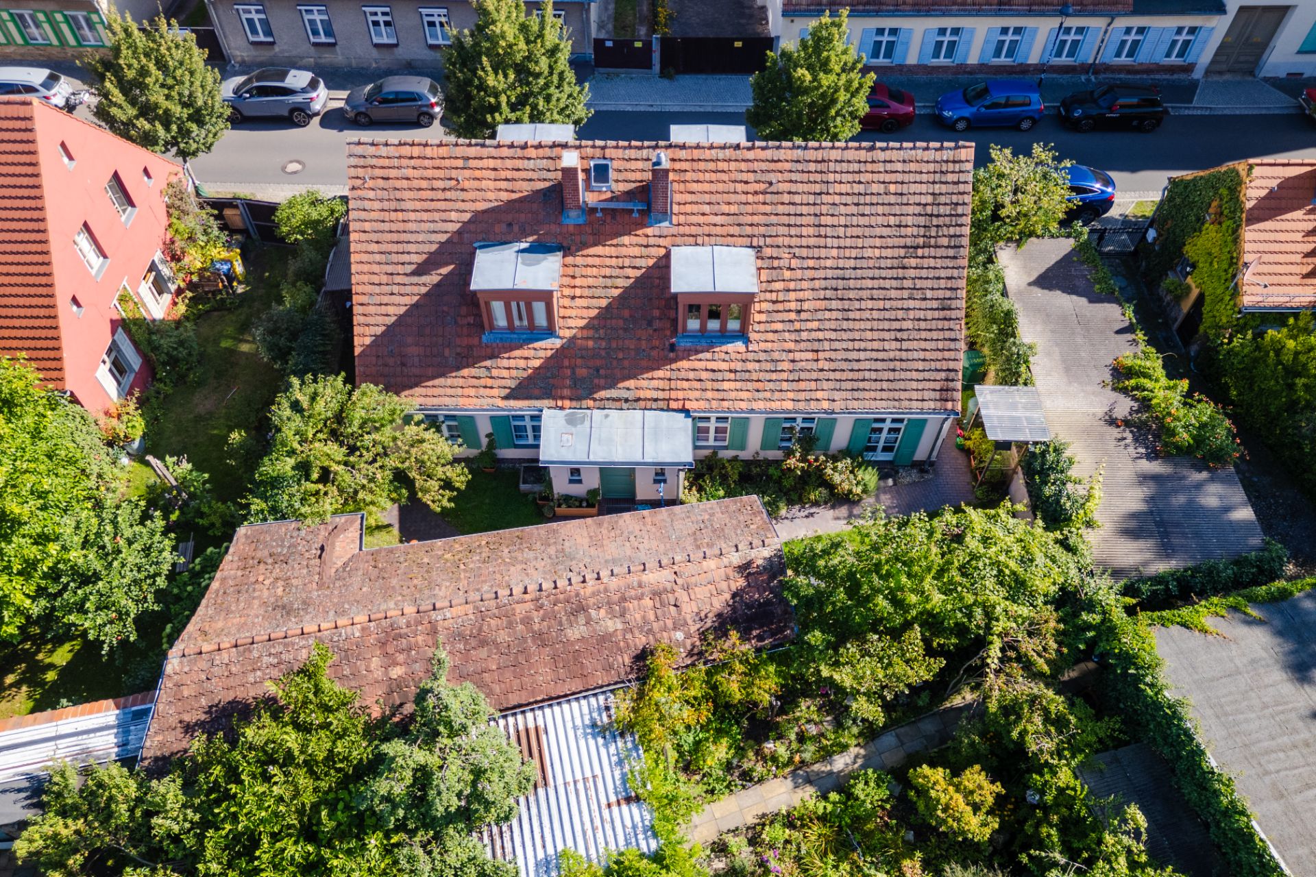 Luftaufnahme eines Wohnhauses mit rotem Dach, Garten und angrenzender Straße.
