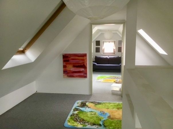 Dachgeschossraum mit Teppich, schrägen Wänden, einem Gemälde und Blick auf ein Sofa im Nebenraum.