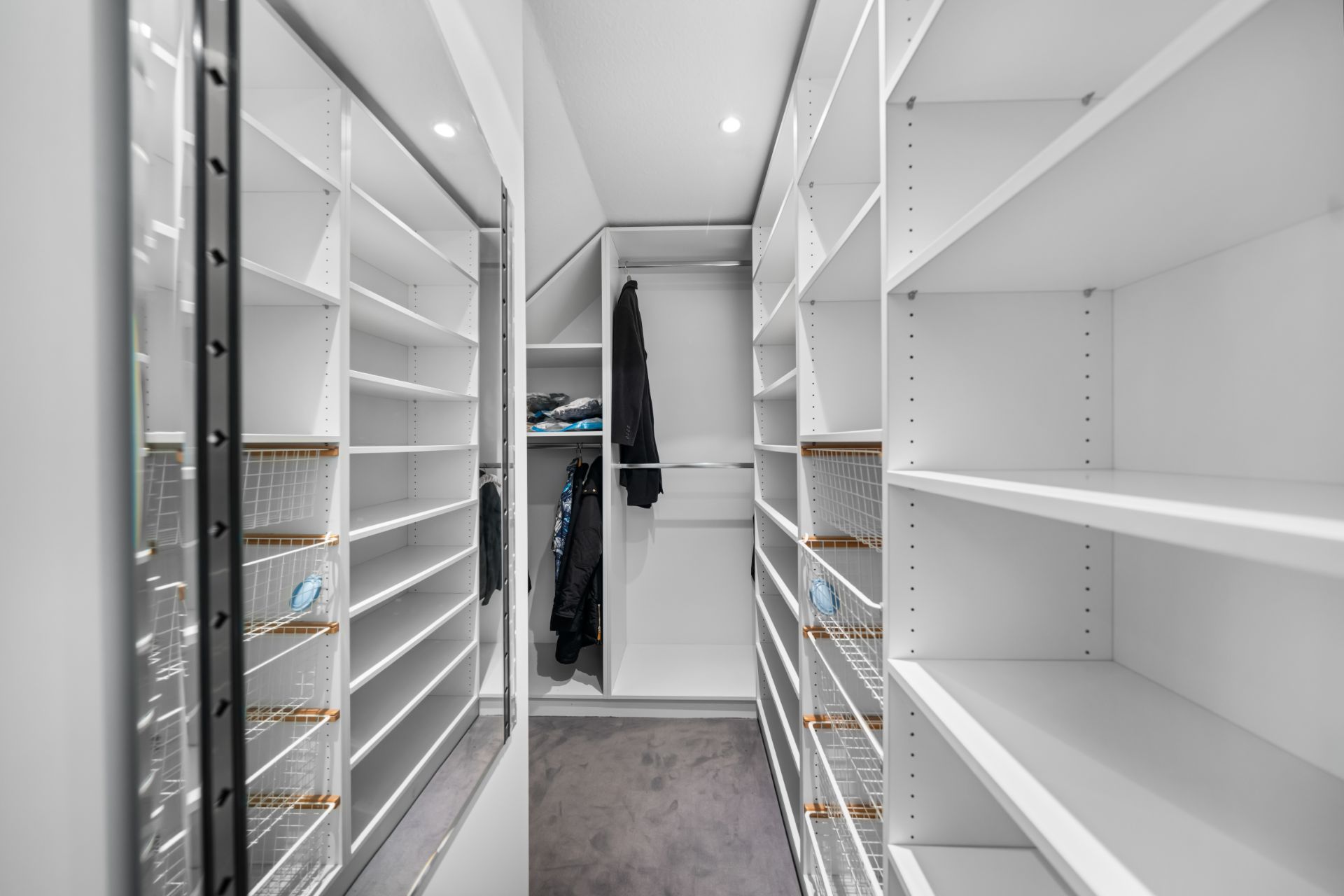 Moderner, weißer begehbarer Kleiderschrank mit Regalen und einigen aufgehängten Jacken.
