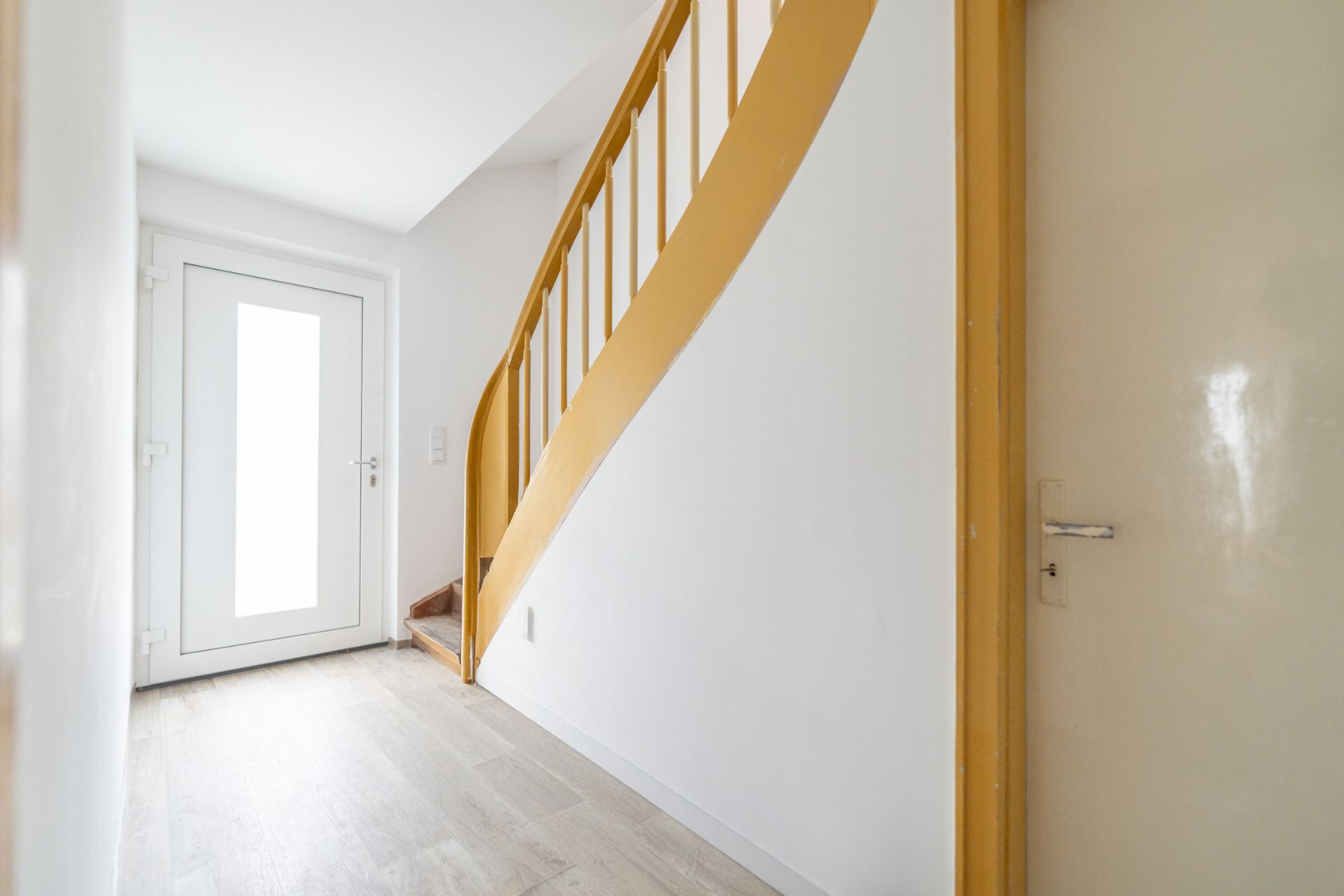 Heller Flur mit weißer Tür und einer gelben Treppe nach oben.