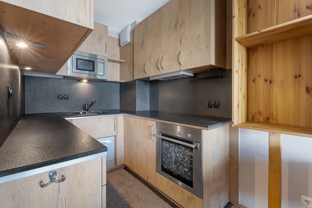 Moderne Einbauküche mit Holzfronten, Backofen, Mikrowelle und offenen Regalen.