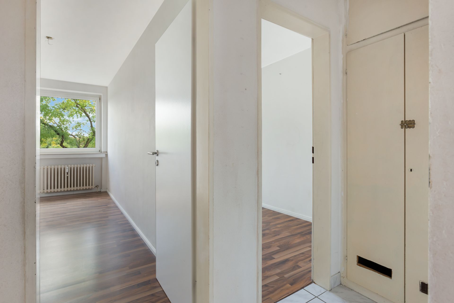 Flur mit zwei offenen Türen, Blick in helle Zimmer mit Holzfußboden und Fenster.