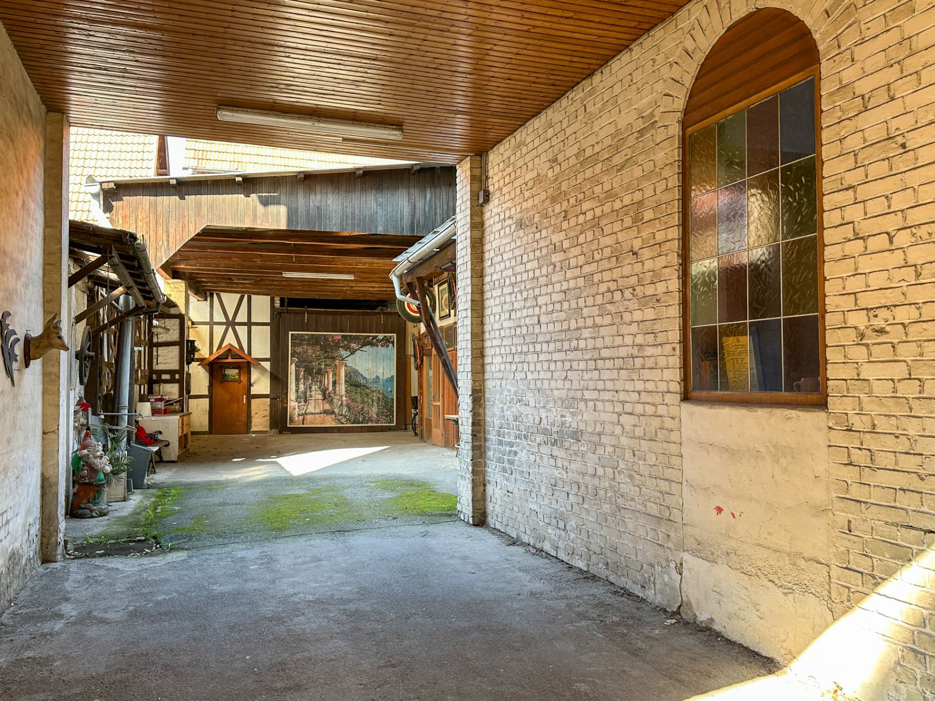 Überdachter Hof mit Backsteinwand und buntem Fenster, im Hintergrund Fachwerk und Tor.