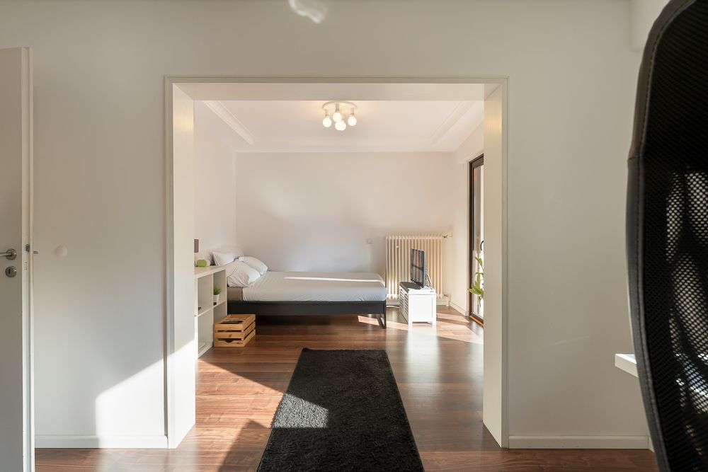 Helles Schlafzimmer mit Doppelbett, Nachttisch, Teppich und Fenster, moderner Holzboden.