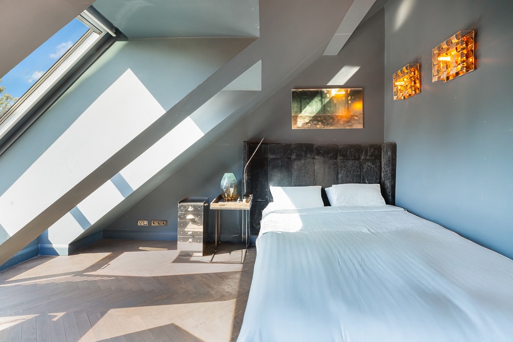 Schlafzimmer mit Doppelbett unter Dachschräge, Nachttisch und Wandlampen.