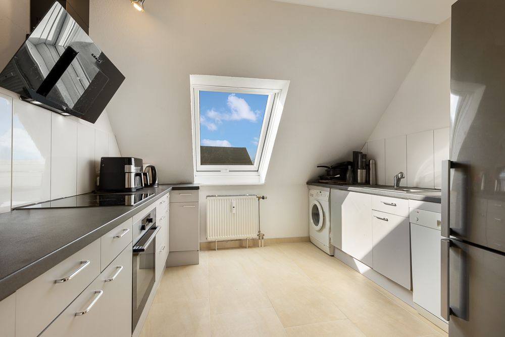 Moderne helle Küche mit Dachfenster, weißen Schränken, Geräten und Waschmaschine.