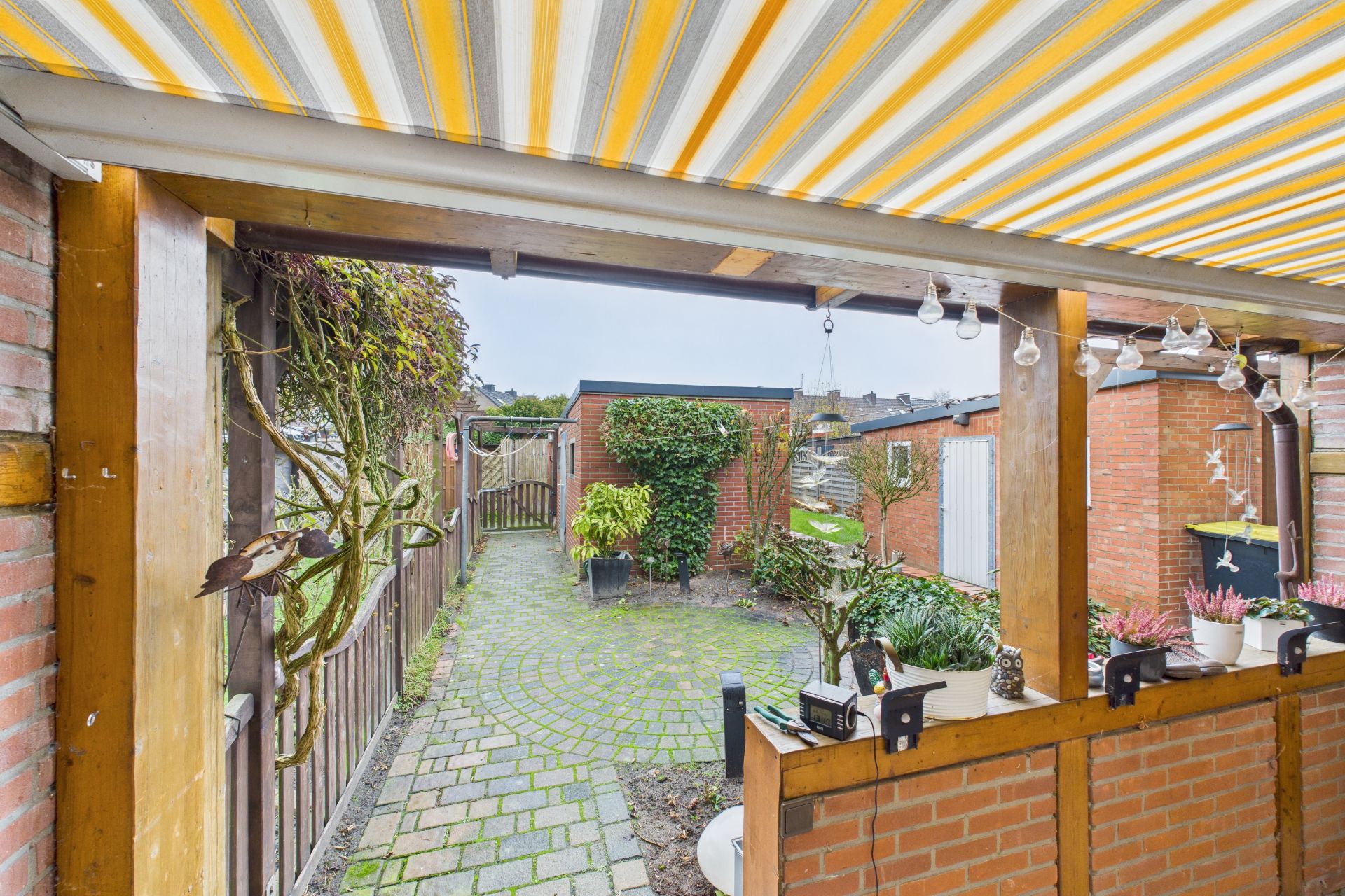 Überdachte Terrasse mit gelb-weiß gestreifter Markise und Blick auf einen begrünten Garten.