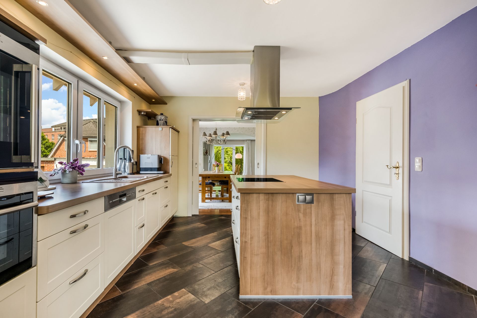 Moderne Küche mit Kücheninsel, hellen Schränken und großen Fenstern, Blick ins Esszimmer.