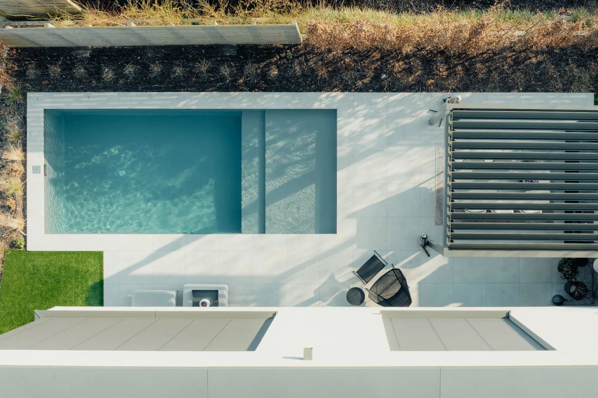 Vogelperspektive auf einen kleinen rechteckigen Pool, Terrasse und zwei Gartenstühle.
