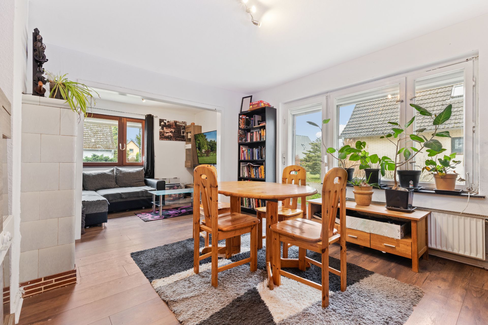 Essbereich mit Holztisch und vier Stühlen, Wohnzimmer mit Sofa, viele Pflanzen am Fenster.