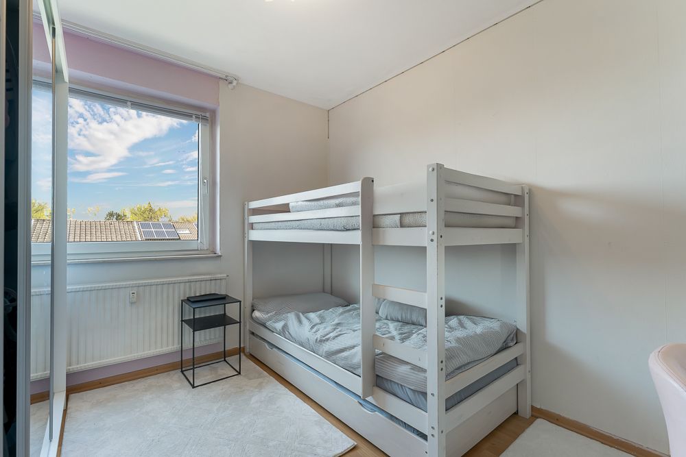 Kleines Zimmer mit Etagenbett, Fenster, Nachttisch und hellem Teppichboden.