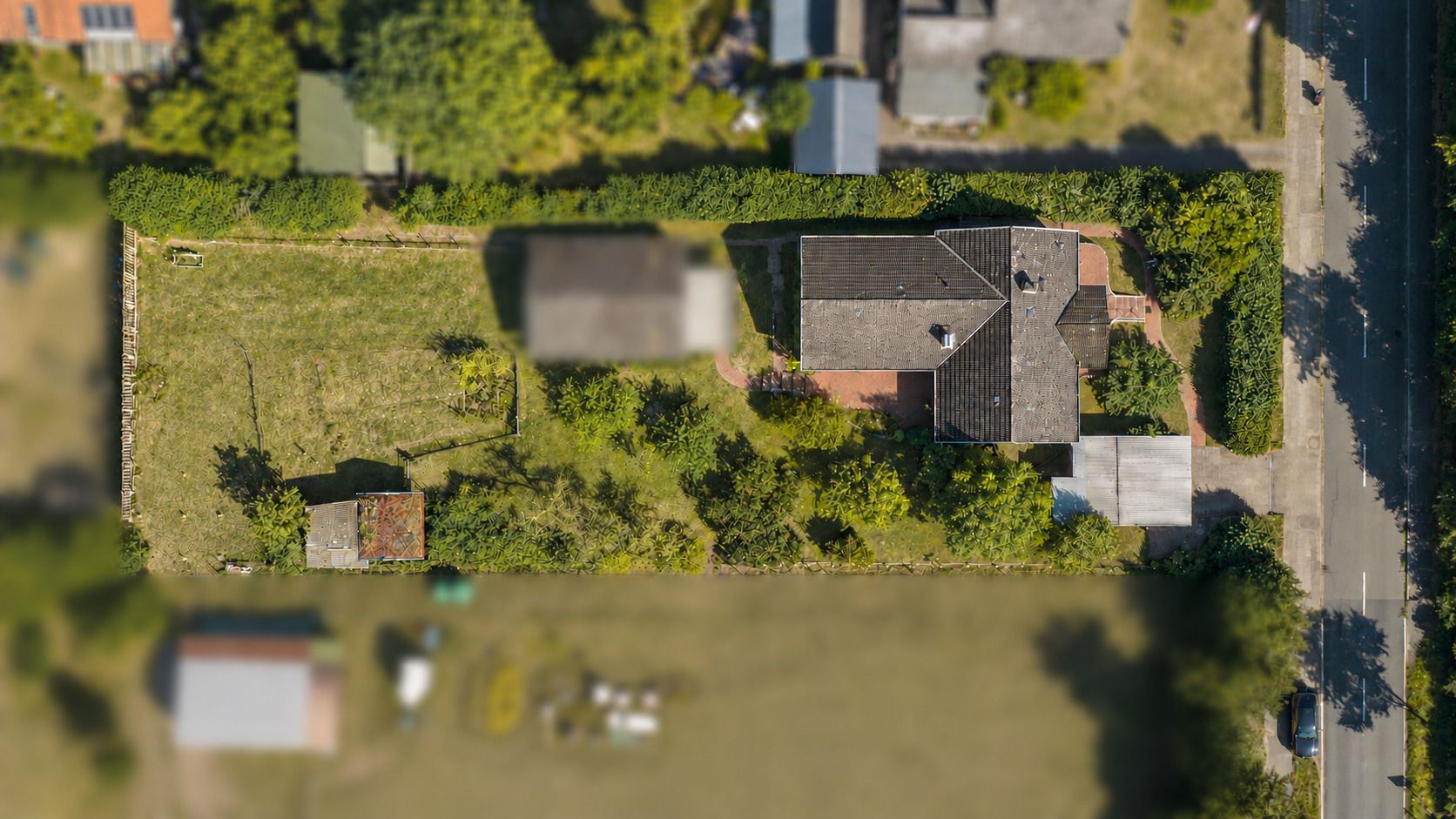 Luftaufnahme eines Wohnhauses mit Garten, Nebengebäuden und umliegenden Bäumen.