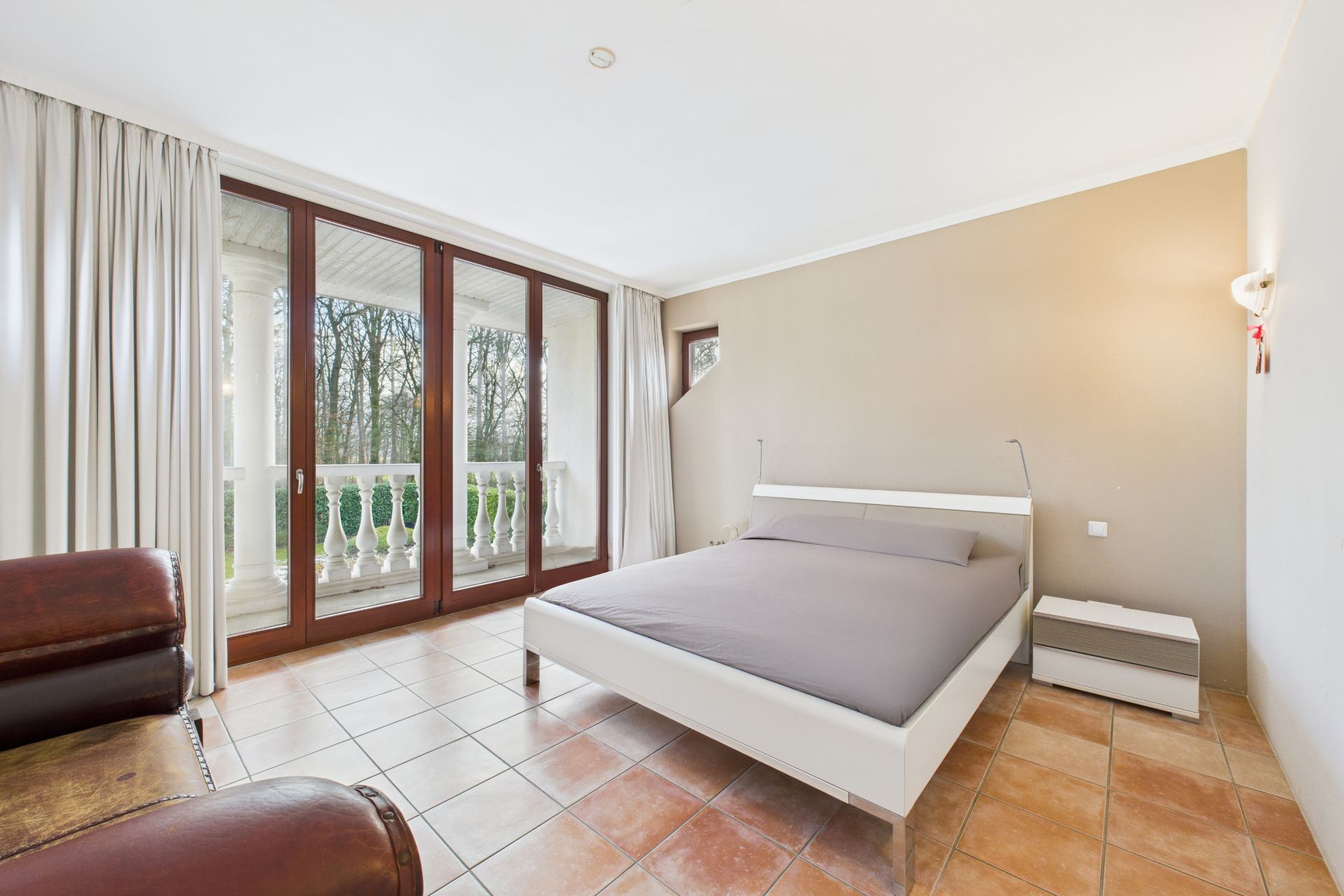 Helles Schlafzimmer mit Doppelbett, Nachttisch, Ledersessel und großen Fenstern zur Terrasse.