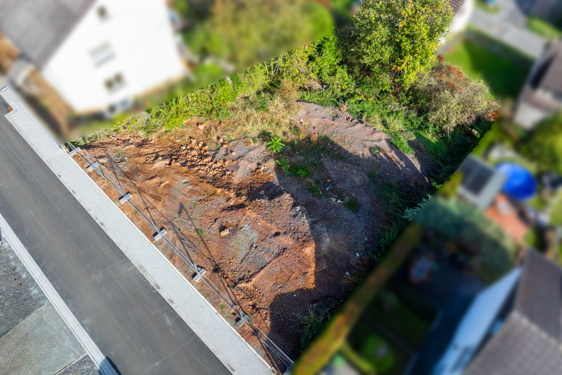 Luftaufnahme eines unbebauten Grundstücks neben einer Straße mit etwas Vegetation am Rand.