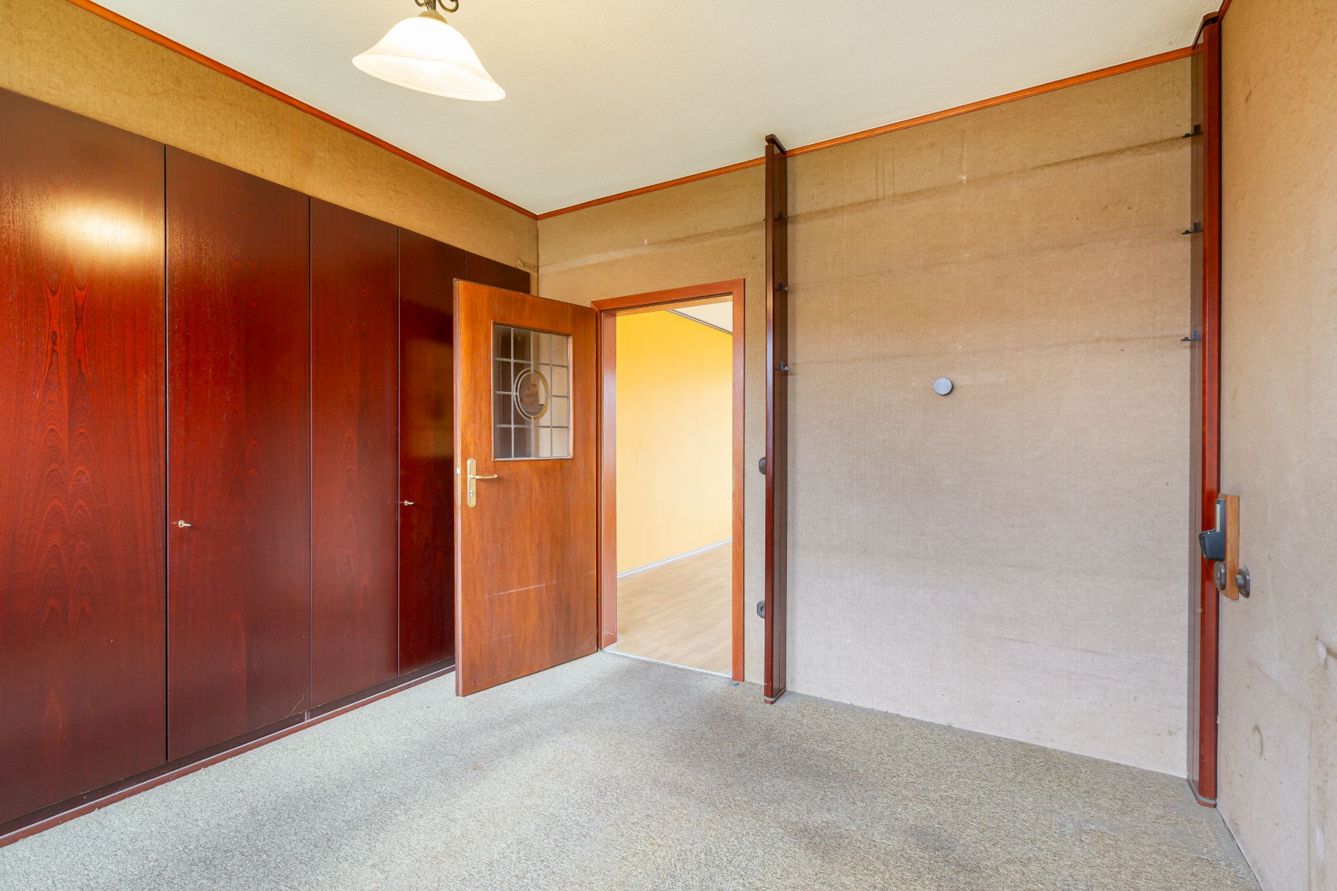 Leerer Raum mit Holztür, Wandschrank und Deckenlampe.