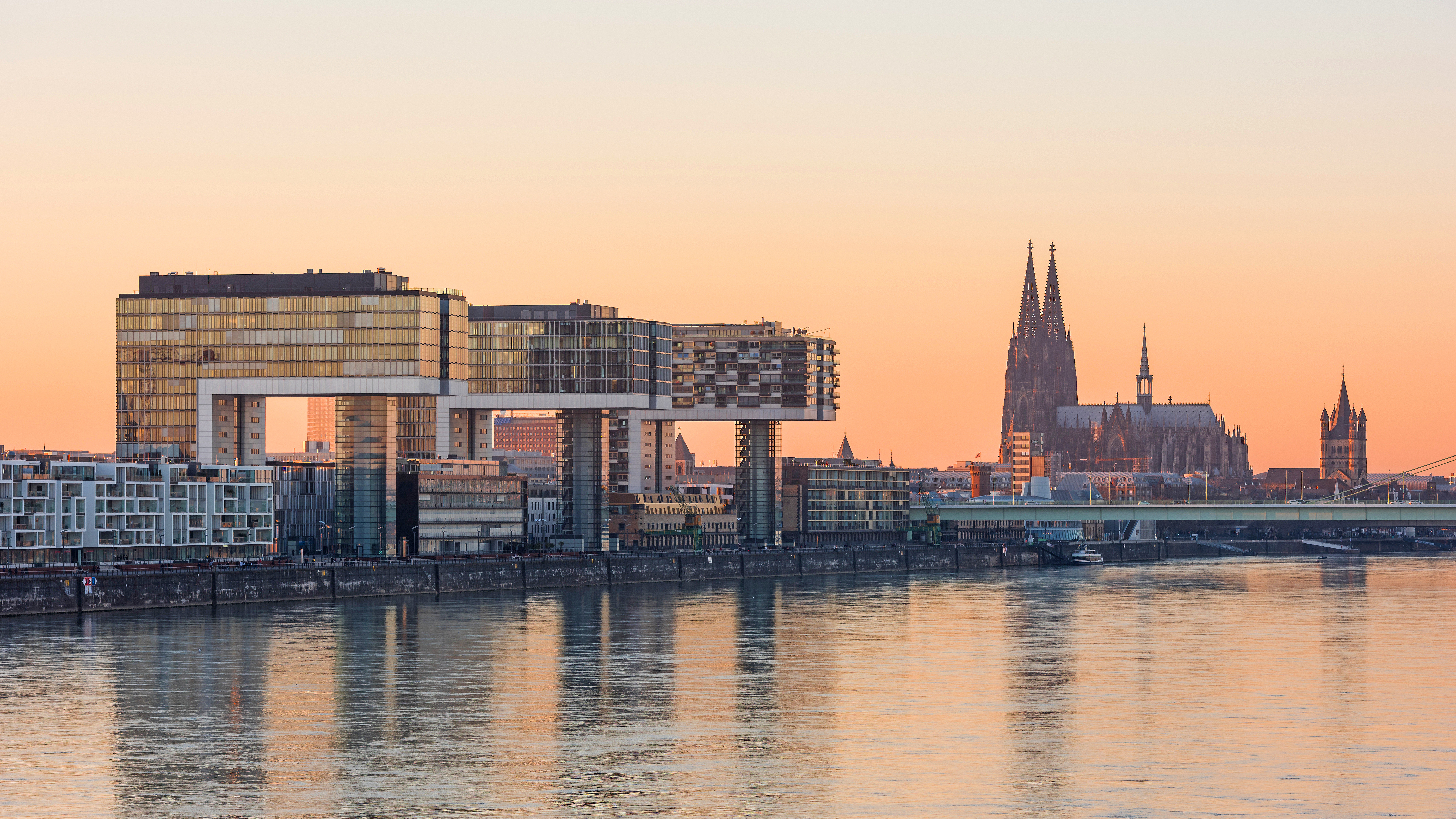 Moderne Wohngebäude am Flussufer, im Hintergrund ein großer Dom bei Sonnenuntergang.