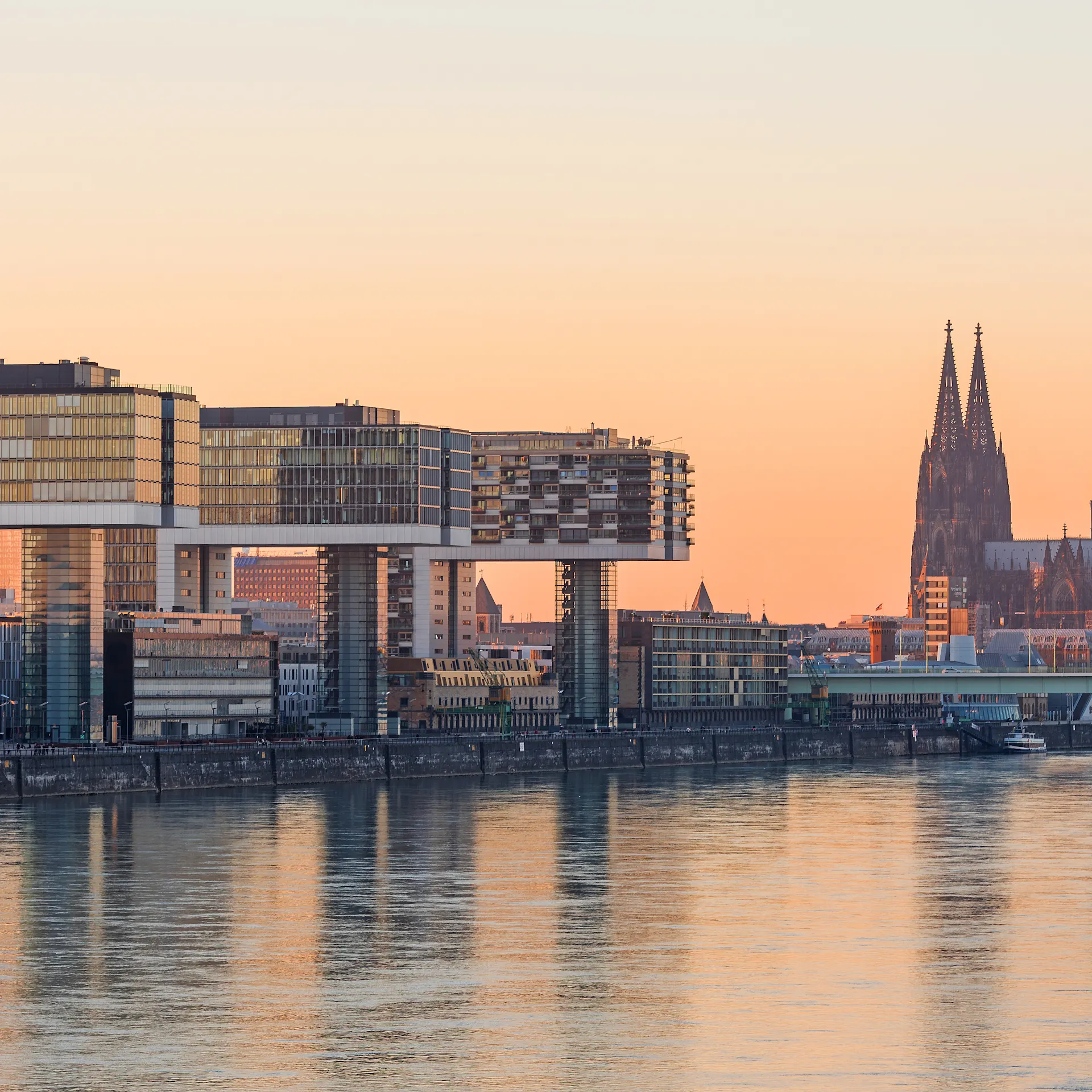Moderne Wohngebäude am Flussufer, im Hintergrund ein großer Dom bei Sonnenuntergang.