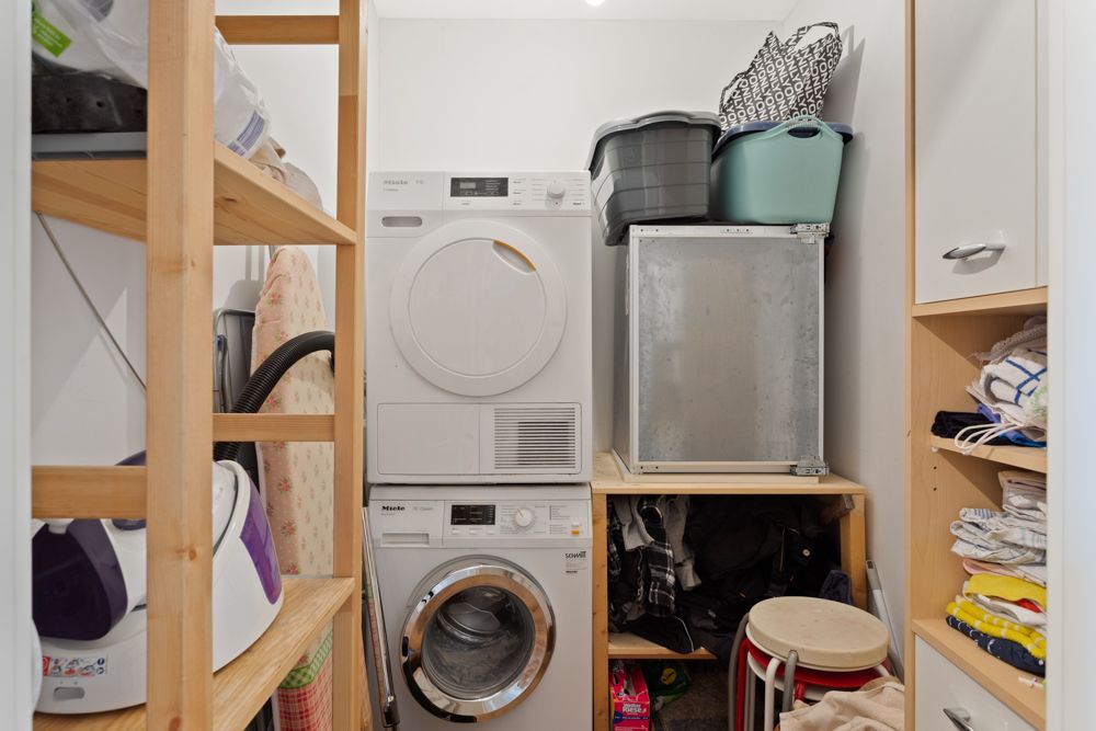 Kleiner Hauswirtschaftsraum mit Waschmaschine, Trockner, Regalen und Haushaltsgegenständen.