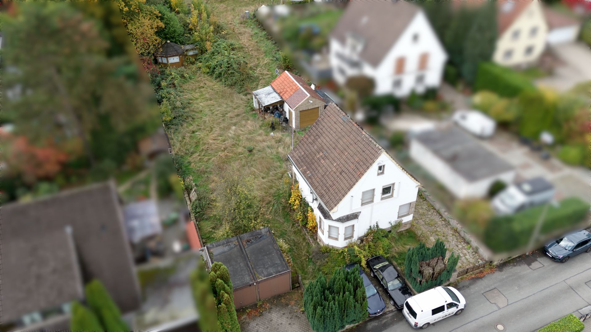 Luftaufnahme eines Einfamilienhauses mit großem Garten und mehreren geparkten Autos davor.