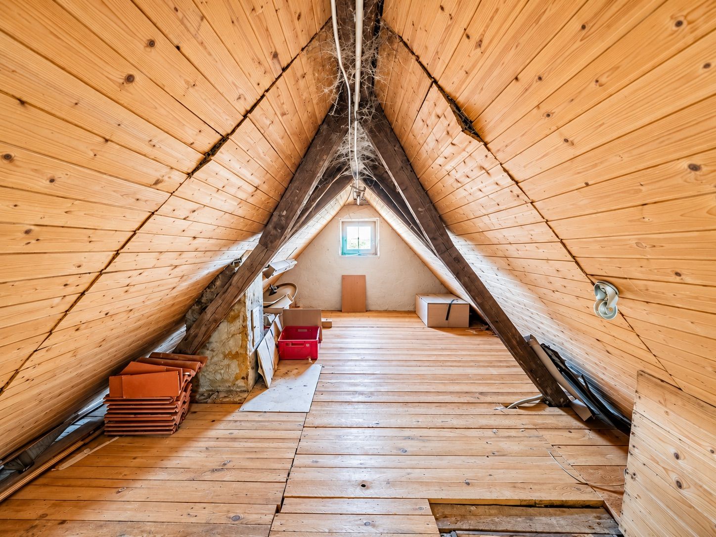 Dachboden mit Holzverkleidung, sichtbaren Balken und einigen gelagerten Kisten.