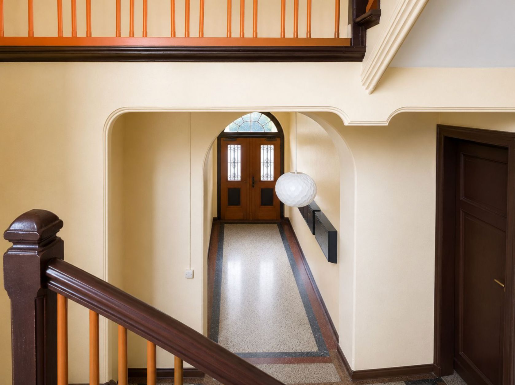 Flur in einem Wohnhaus mit Treppenhaus, Holztür und runder Lampe an der Decke.