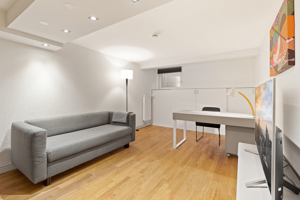 Modernes Zimmer mit grauem Sofa, Schreibtisch, Fernseher und Stehlampe auf Holzfußboden.