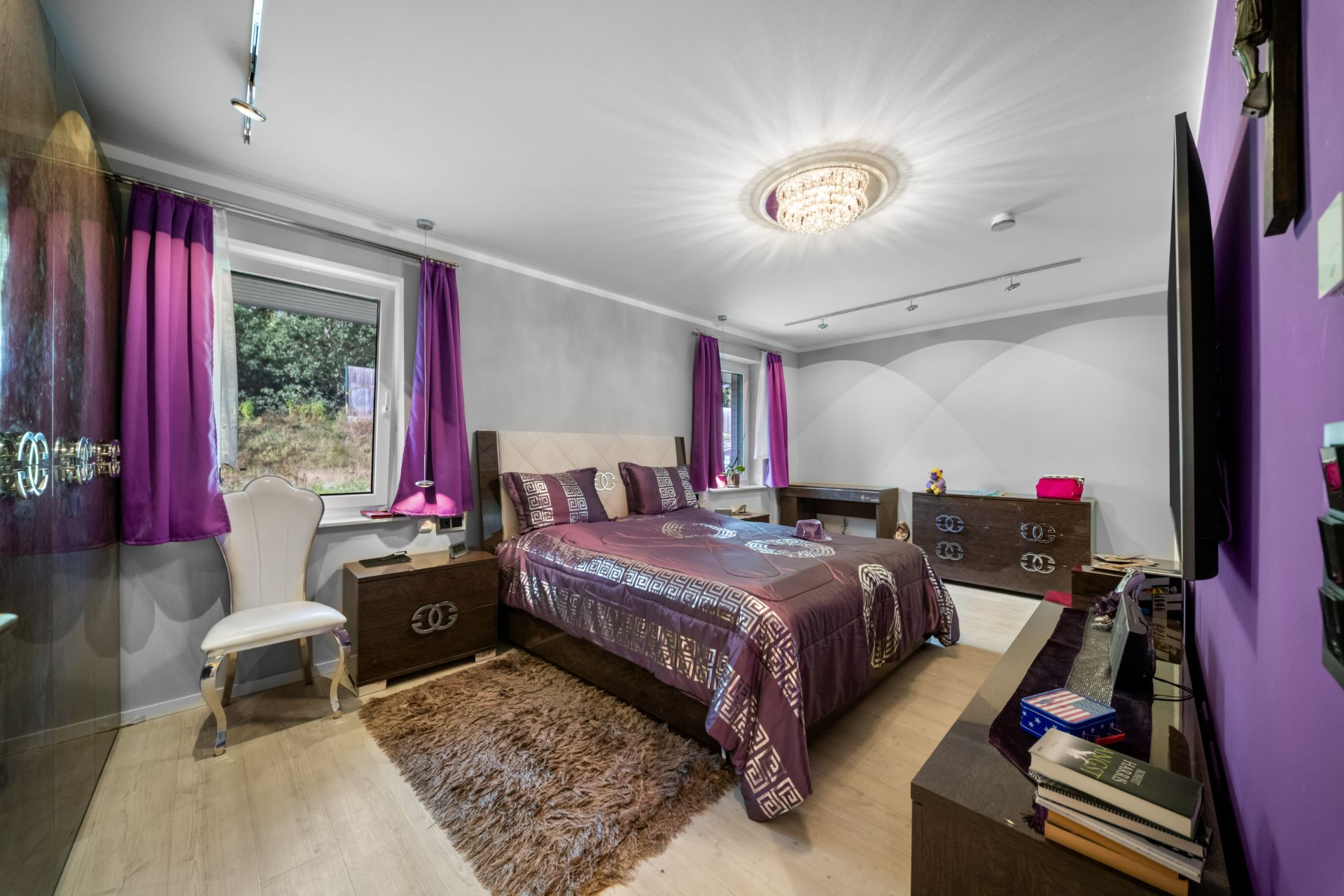 Modernes Schlafzimmer mit Doppelbett, lila Vorhängen, Teppich und großem Fenster.